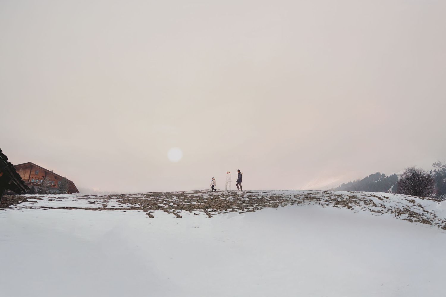 Two people standing on snowy landscape at dusk with glowing sun on overcast winter horizon.