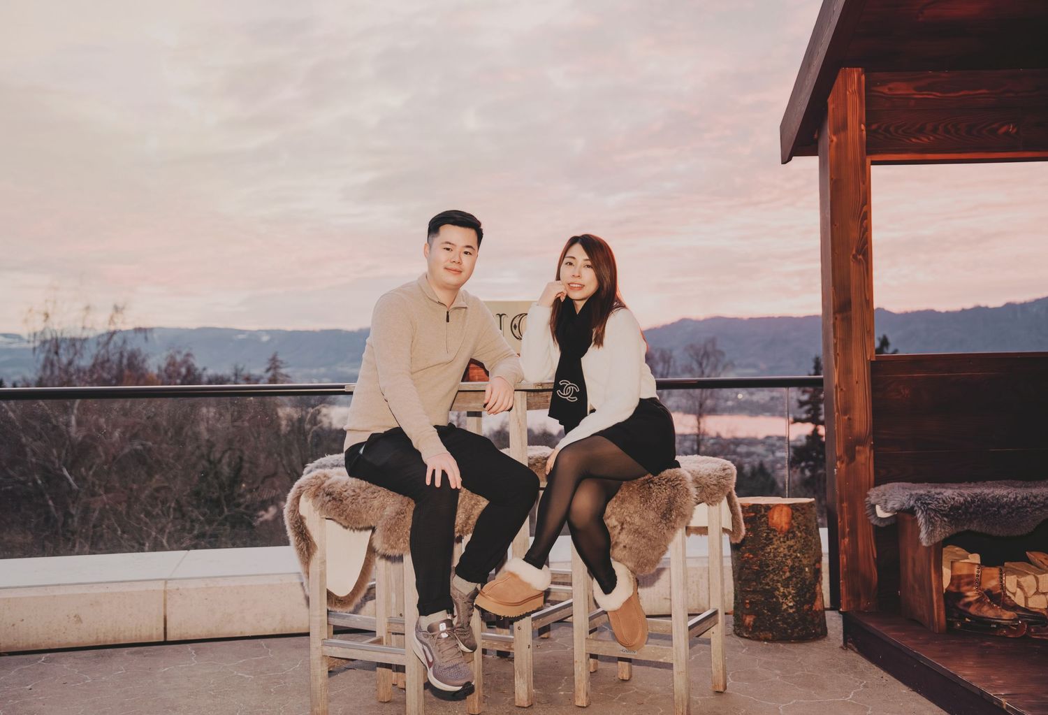 Couple sitting together on terrace at sunset with scenic landscape and fireplace in background.