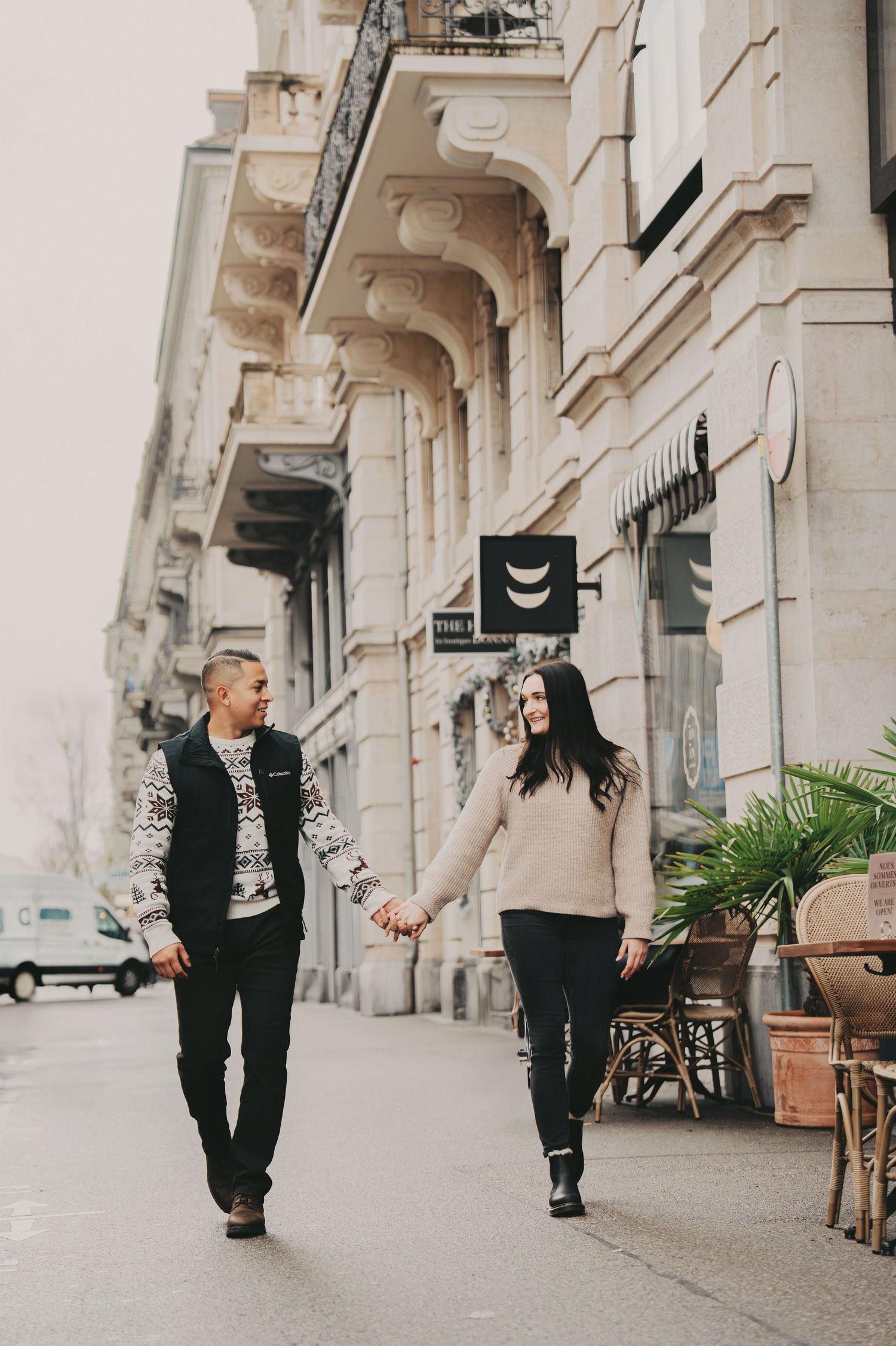 Stylish couple walking hand in hand along a grand European city street together.