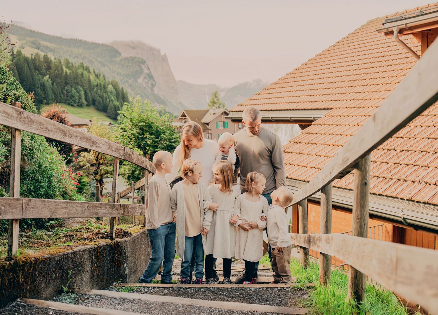 Family of ten posing together on stone steps surrounded by Alpine village homes and mountains.