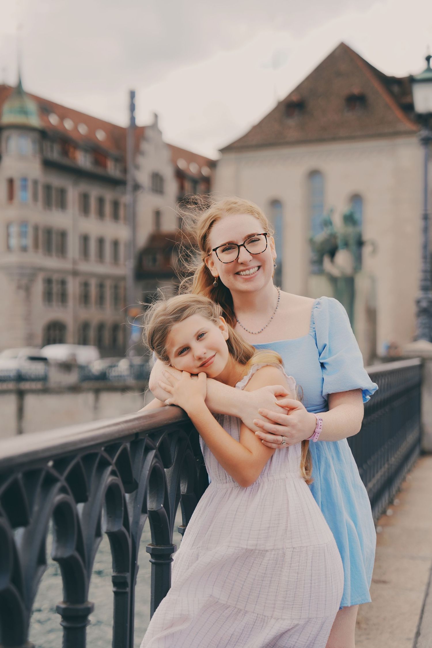 A smiling redhead mother hugs her blonde daughter on a bridge in Zurich old town, Switzerland.