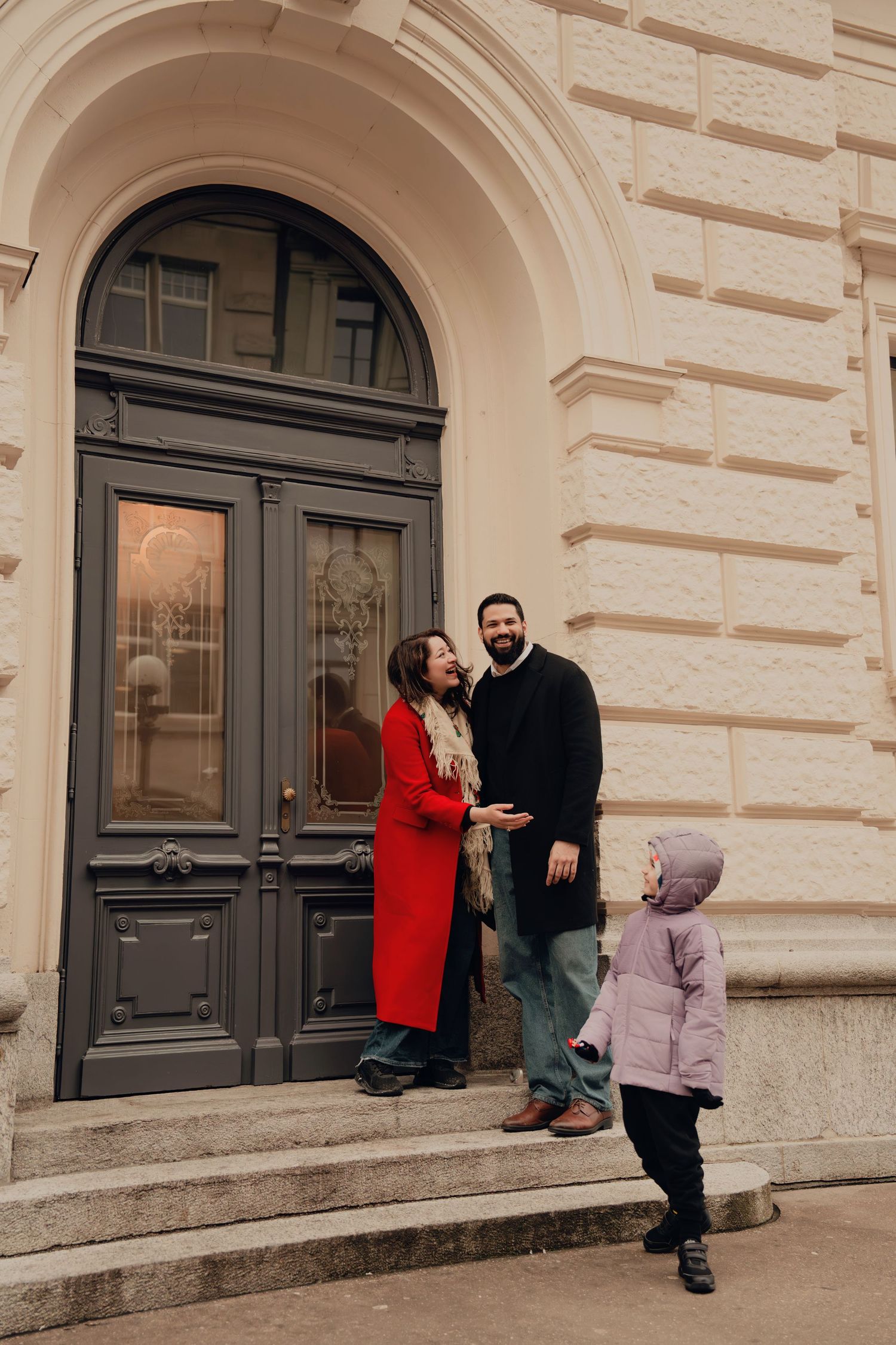 Family laughs together at the entrance of an elegant stone building with arched doorway.