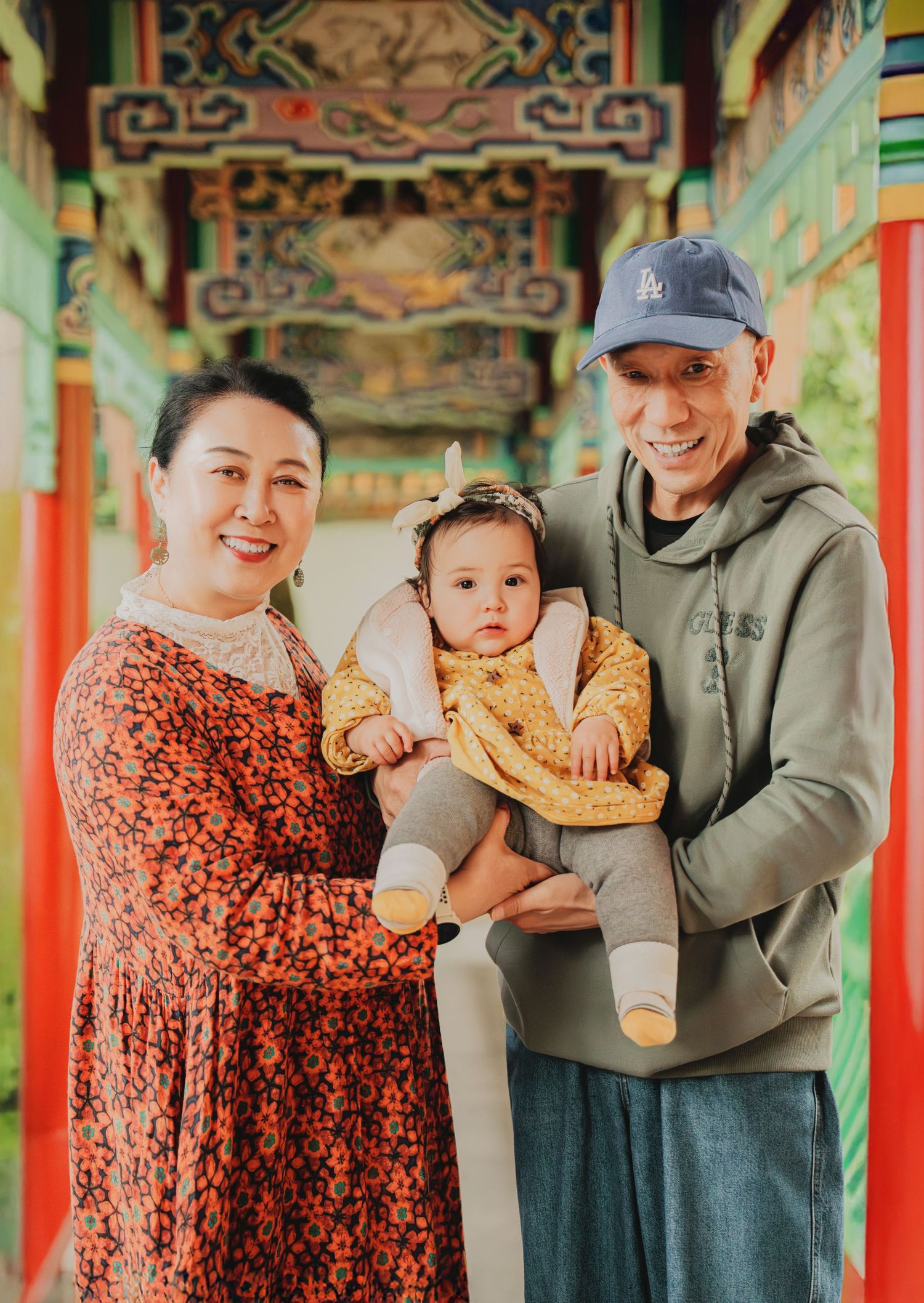 Family portrait of grandparents holding a baby girl in a vibrant Chinese corridor.