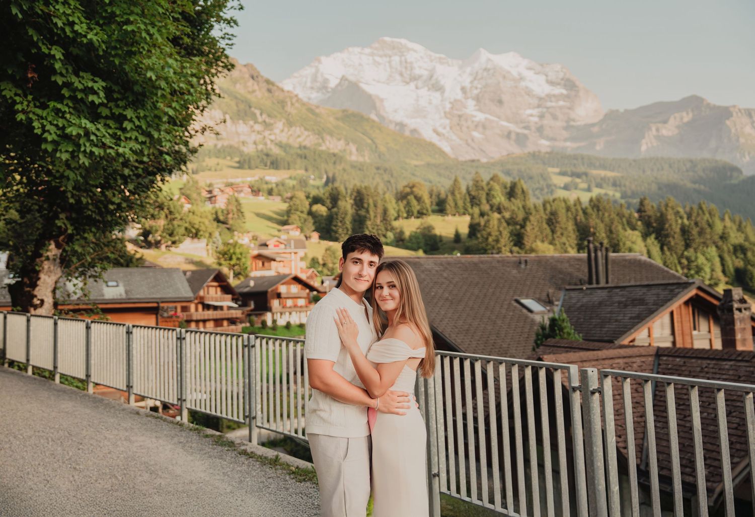 Young couple cuddling together on a terrace with breathtaking snow-capped Swiss Alpine mountain panorama backdrop.