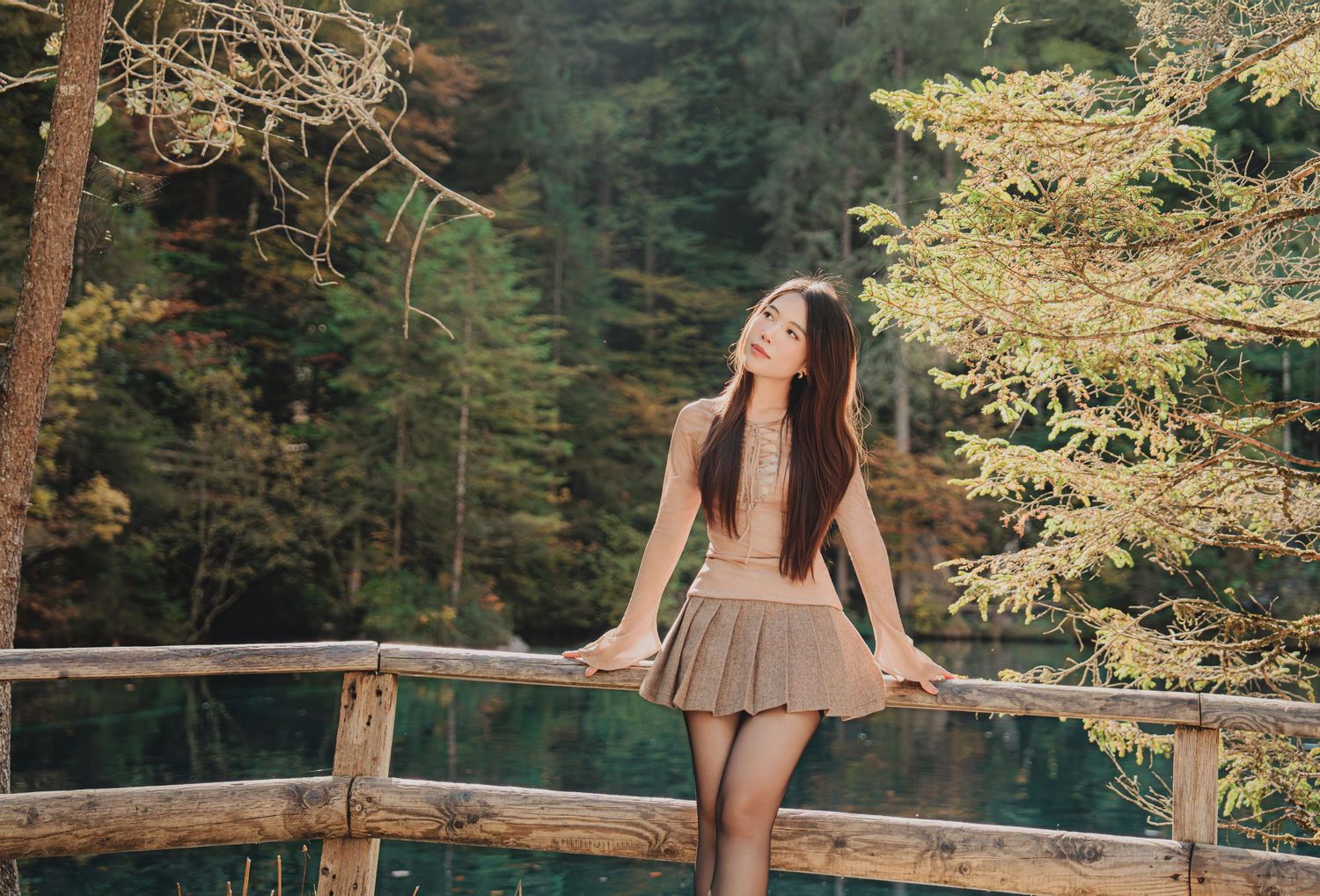 Young woman in mini skirt posing on wooden bridge surrounded by autumn forest trees.