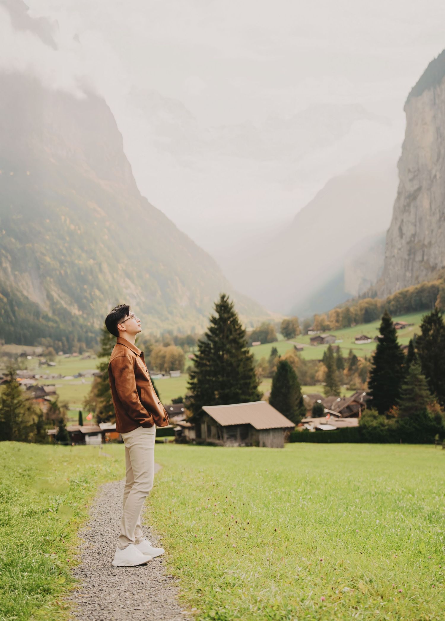 Man in brown jacket looking up at dramatic misty mountain valley in a Swiss alpine landscape.