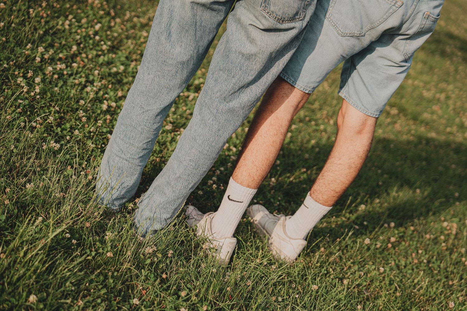 Close-up of two people standing on green grass wearing jeans and white sneakers.