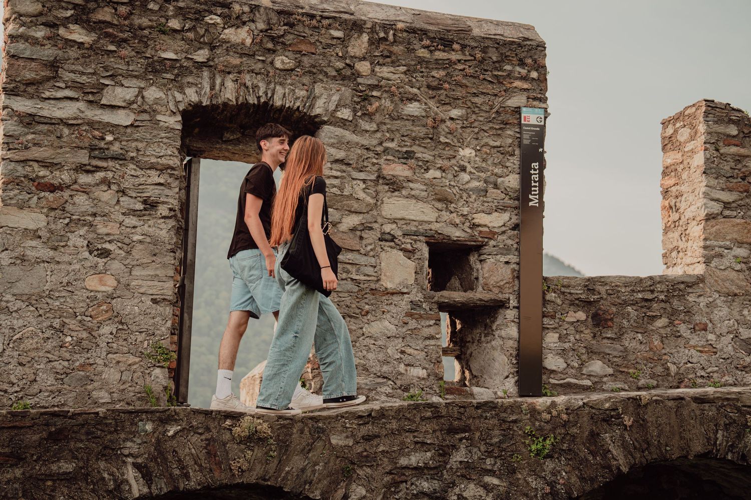 A young couple sharing a kiss in a rustic stone archway doorway of an ancient castle ruin.