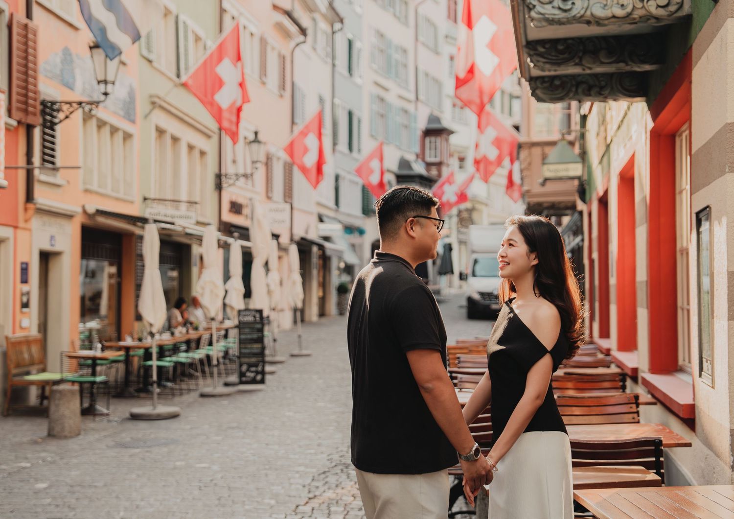 Couple sharing a romantic moment on a quaint European street corner adorned with Swiss flags.