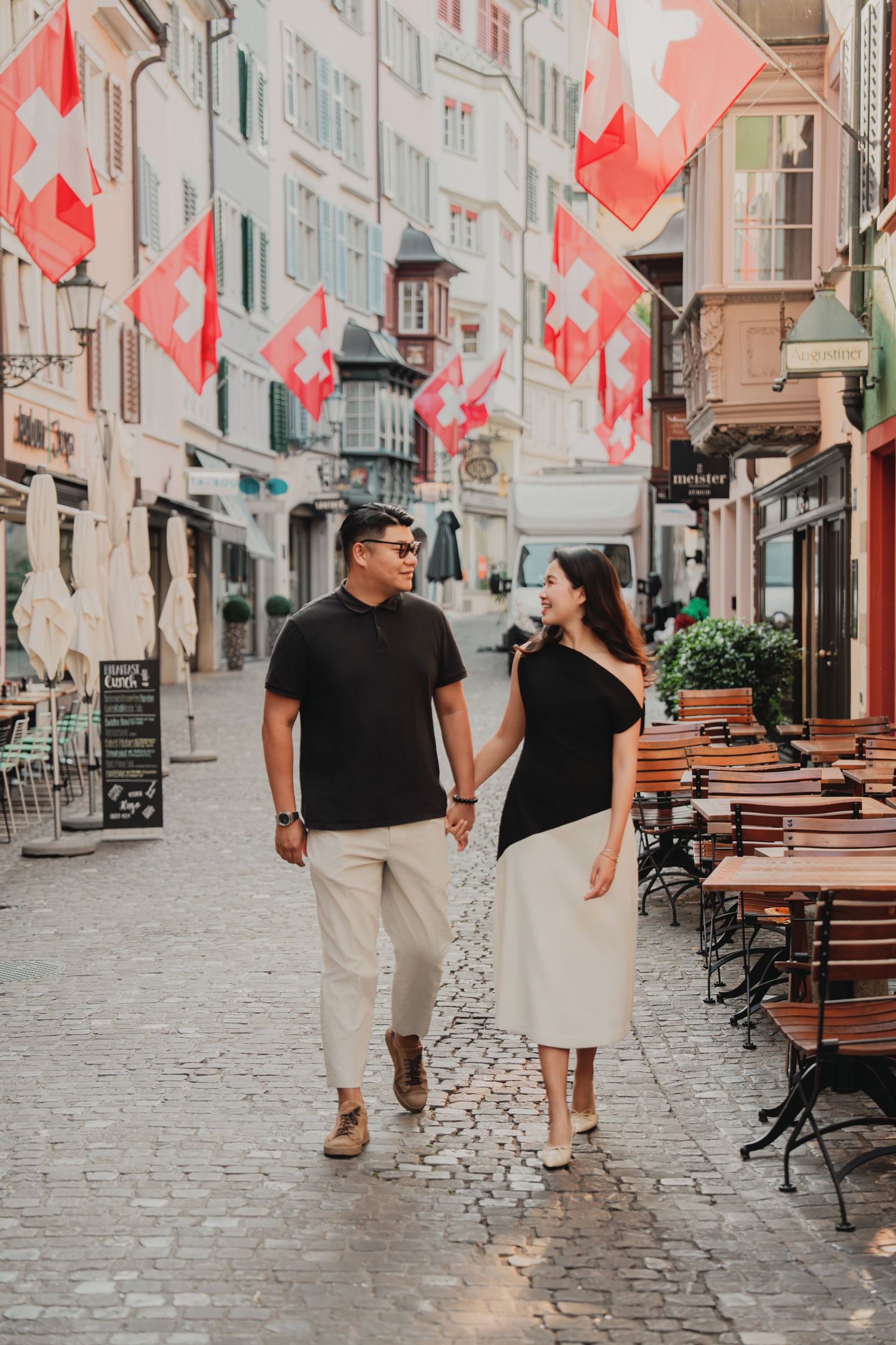 Couple strolling hand in hand through a picturesque Zurich street decorated with Swiss national flags.