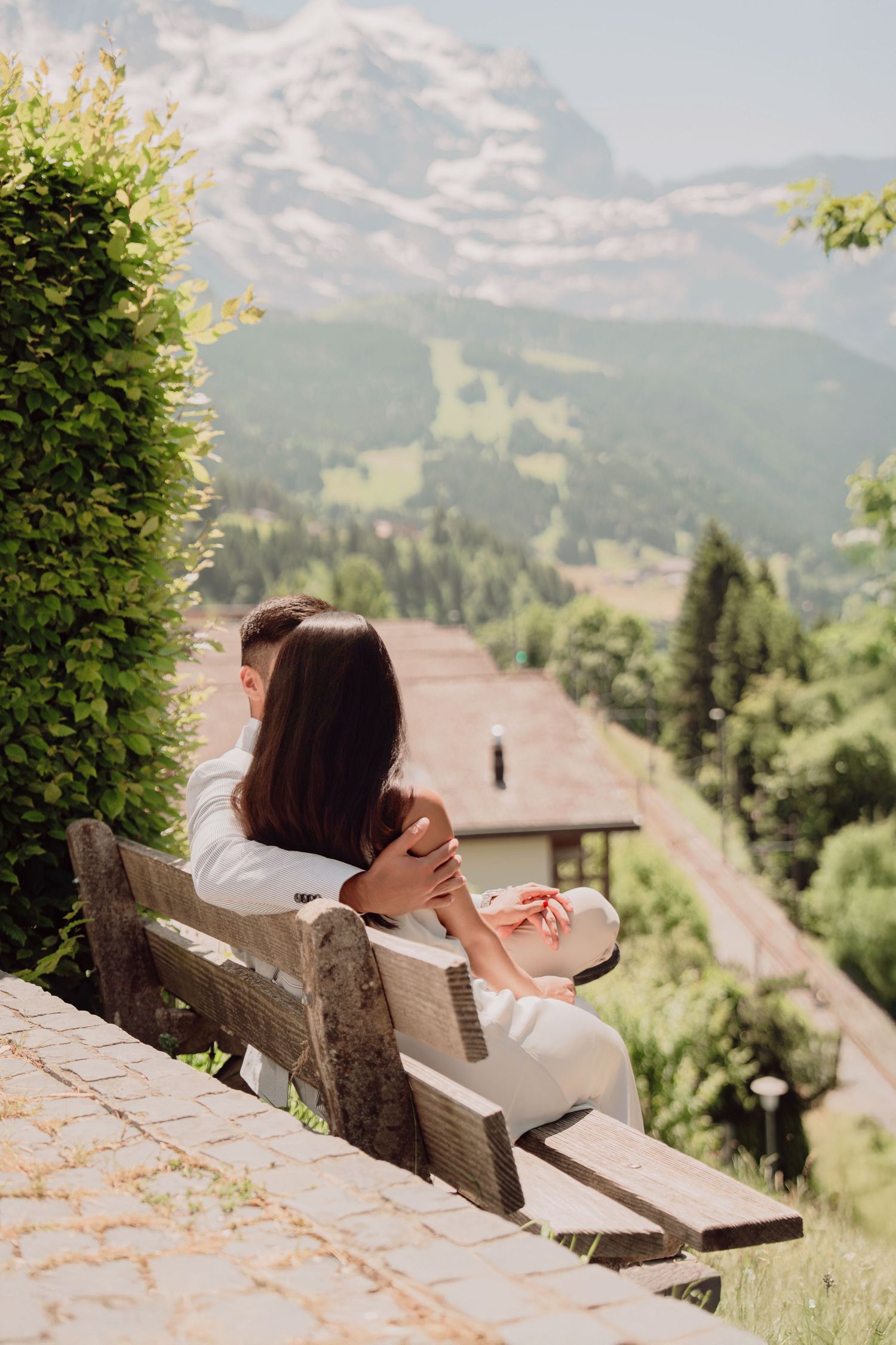 Romantic couple holding hands on a bench overlooking a breathtaking Swiss mountain landscape.