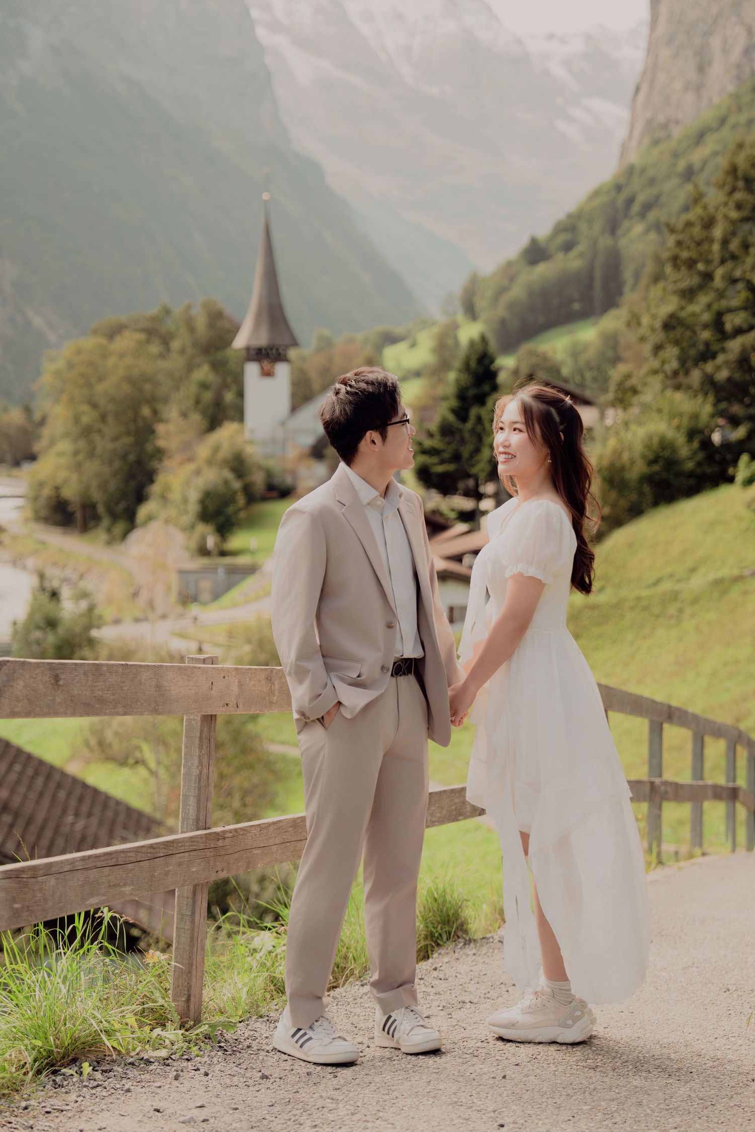 Couple holding hands on a scenic path in Lauterbrunnen Switzerland with alpine village and church backdrop.