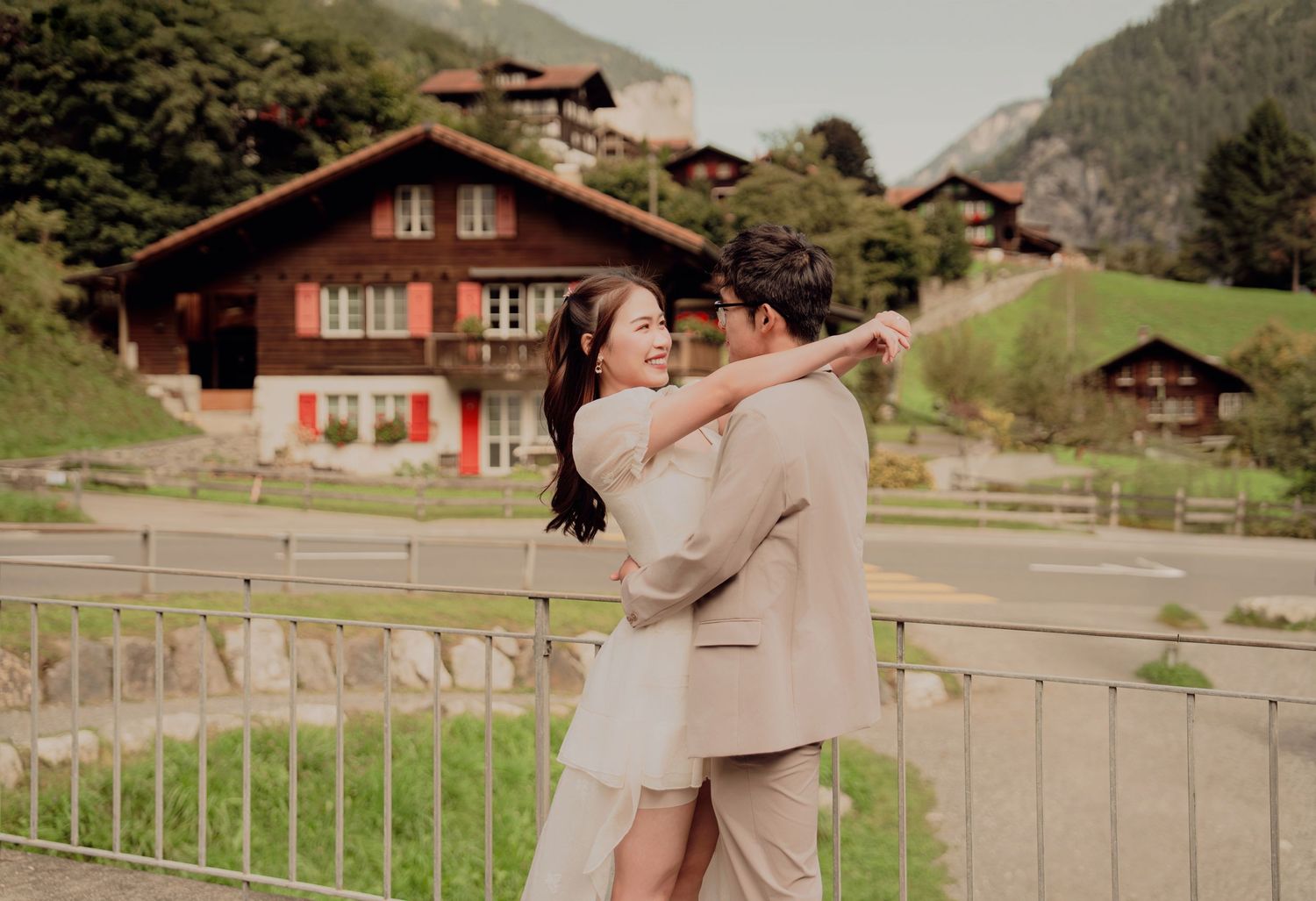 Couple dancing and laughing on a bridge with Swiss chalet homes in the background.