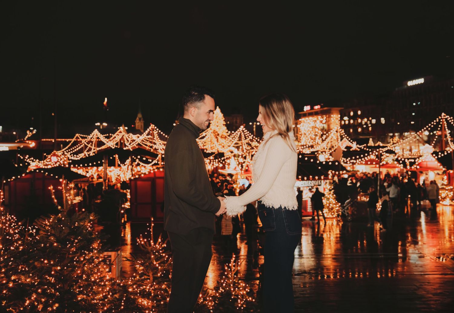 Couple holding hands at romantic night Christmas market with warm golden lights.