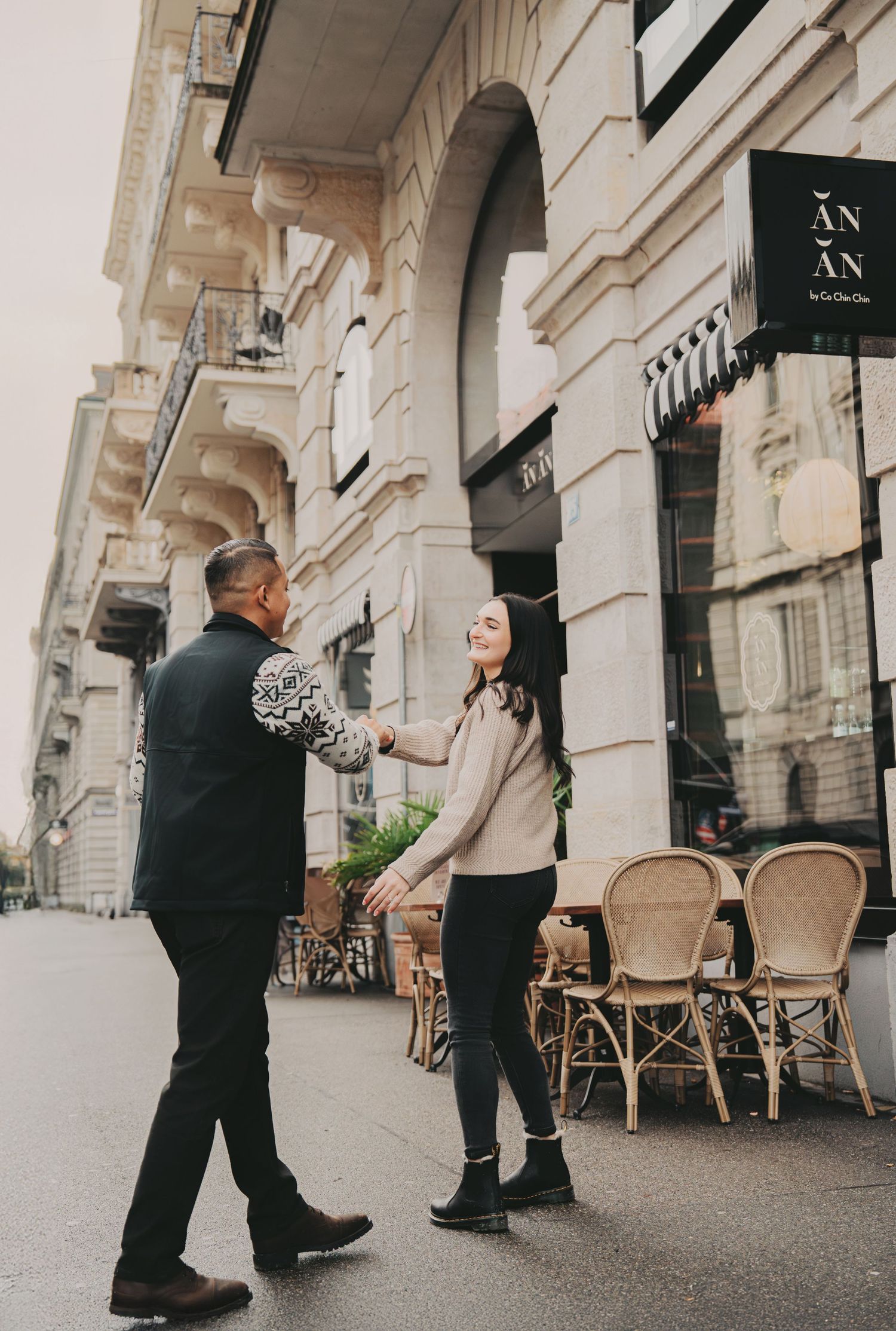 Couple laughing and holding hands outside AN AN restaurant on a European city street.