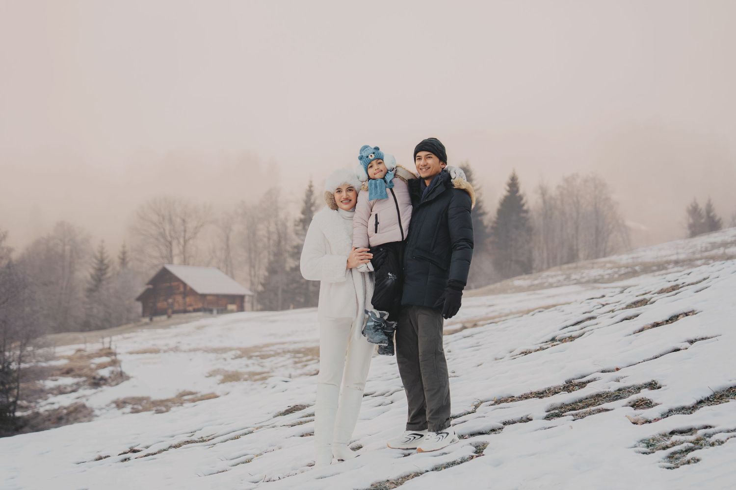 Family of three posing on snowy hillside in foggy winter weather.