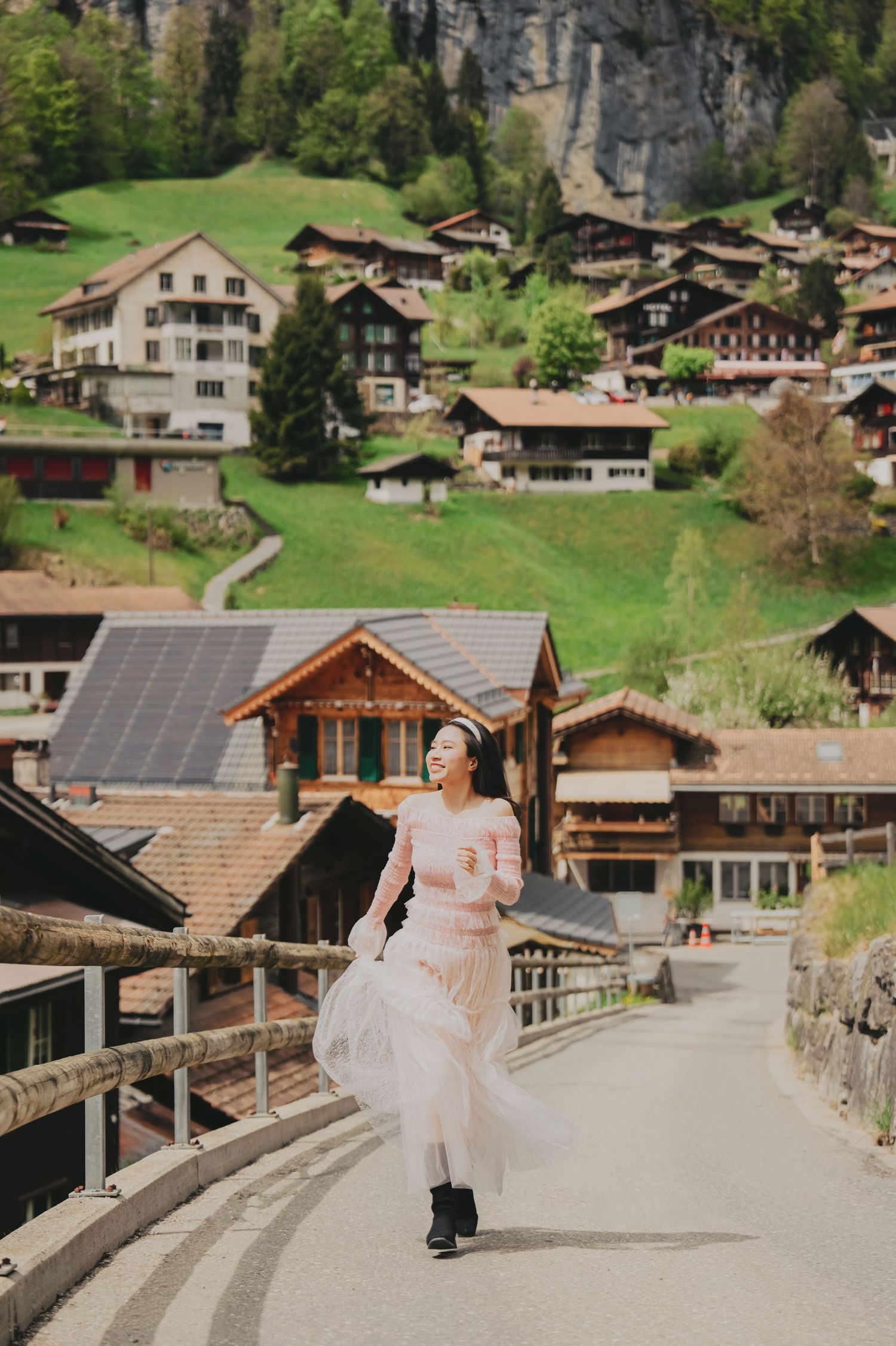 Young woman in flowing pink dress strolling along bridge in picturesque Swiss village of Lauterbrunnen.