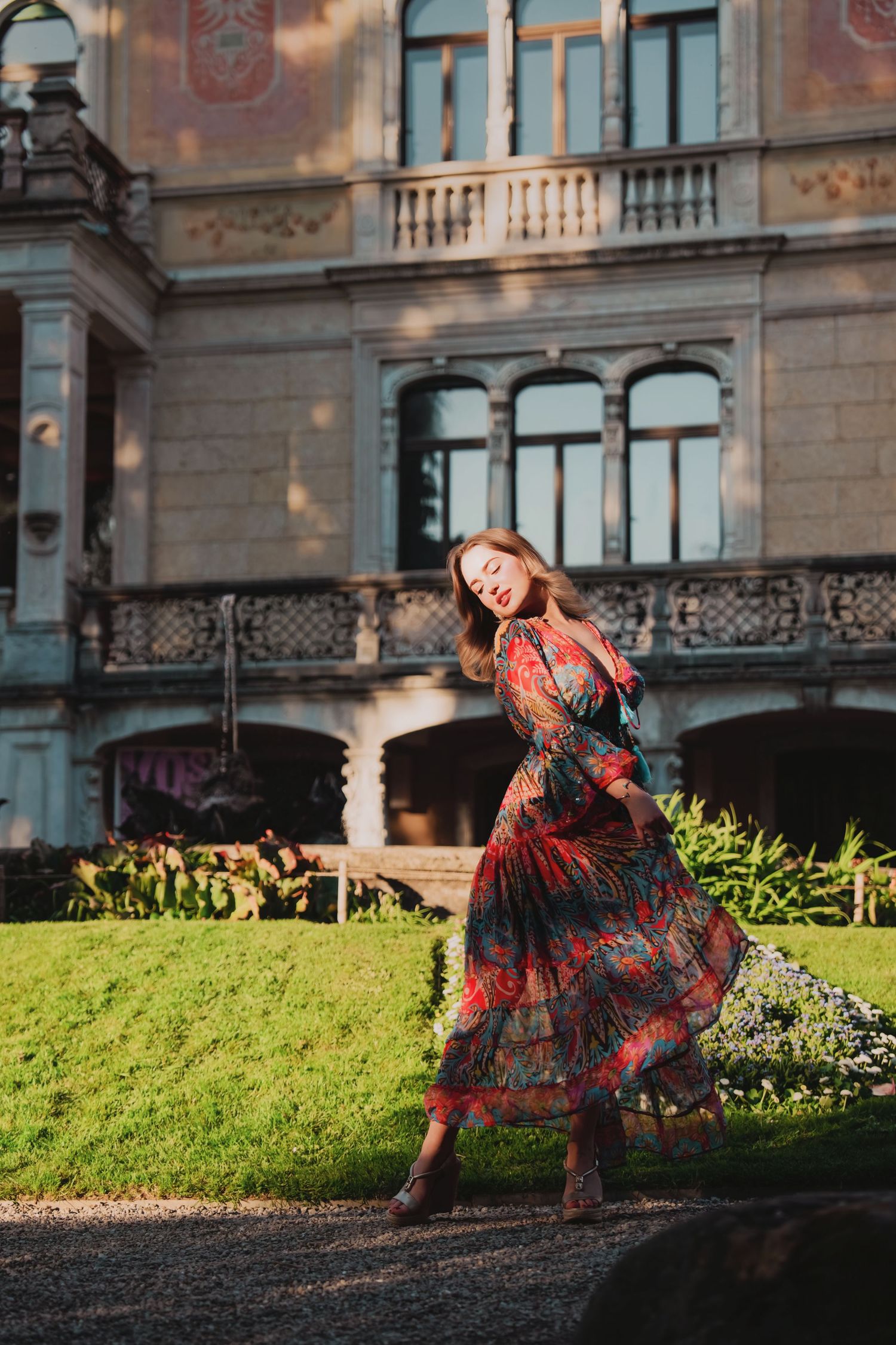 Woman in colorful floral dress twirling before ornate historic building facade.