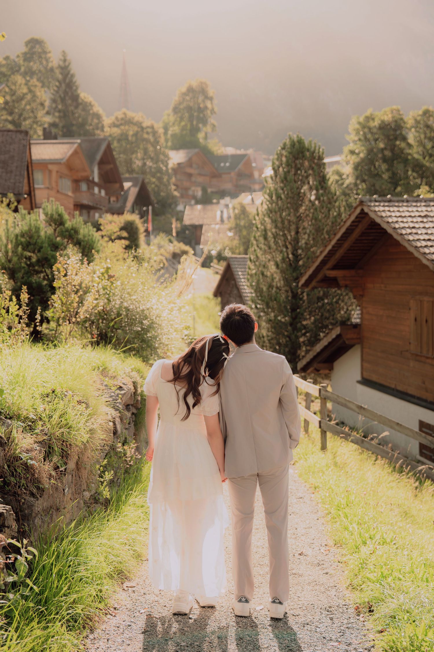 Bride and groom holding hands on a scenic path overlooking a charming Swiss alpine village.