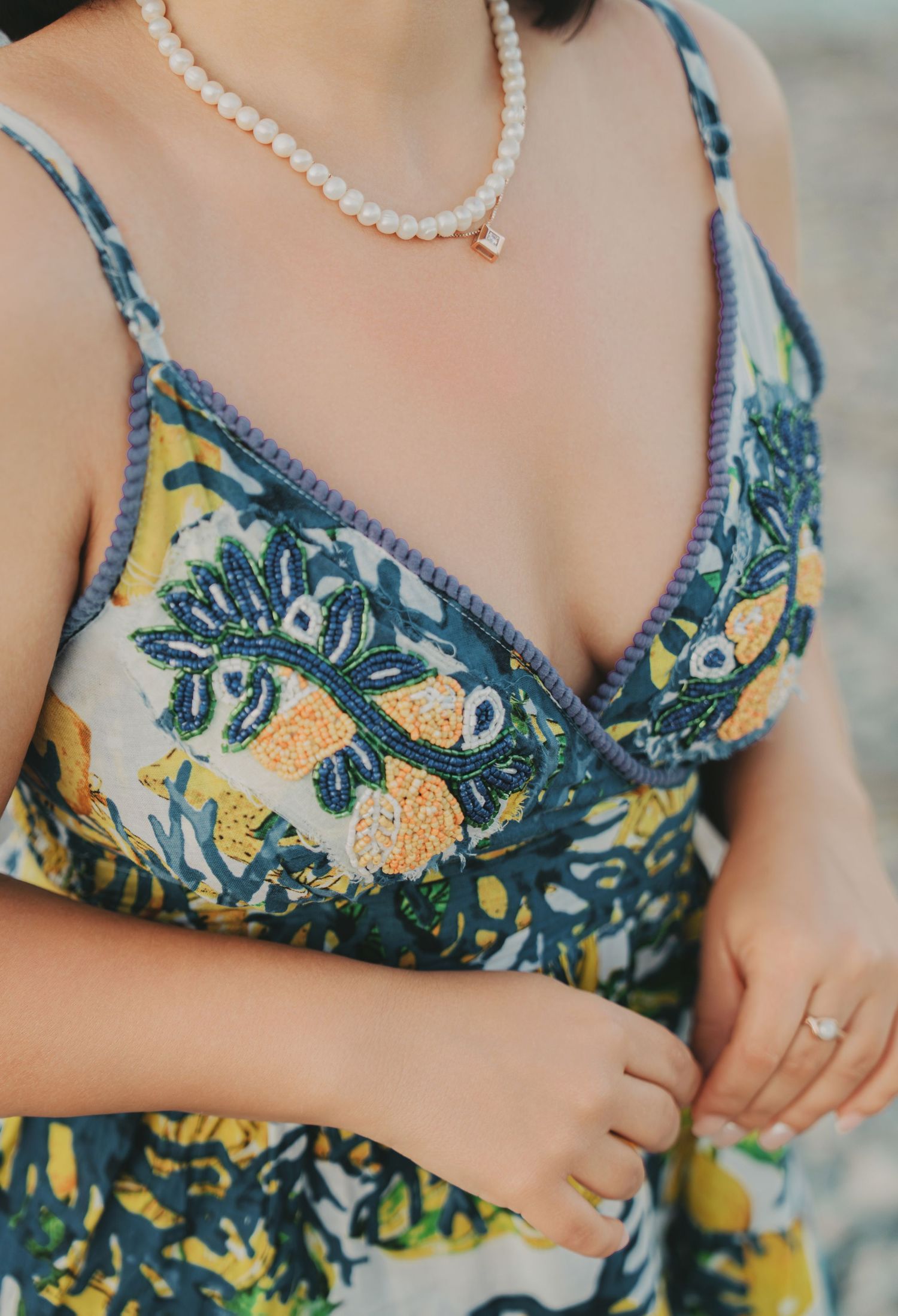 Close-up of embroidered floral sundress with pearl necklace at beach.
