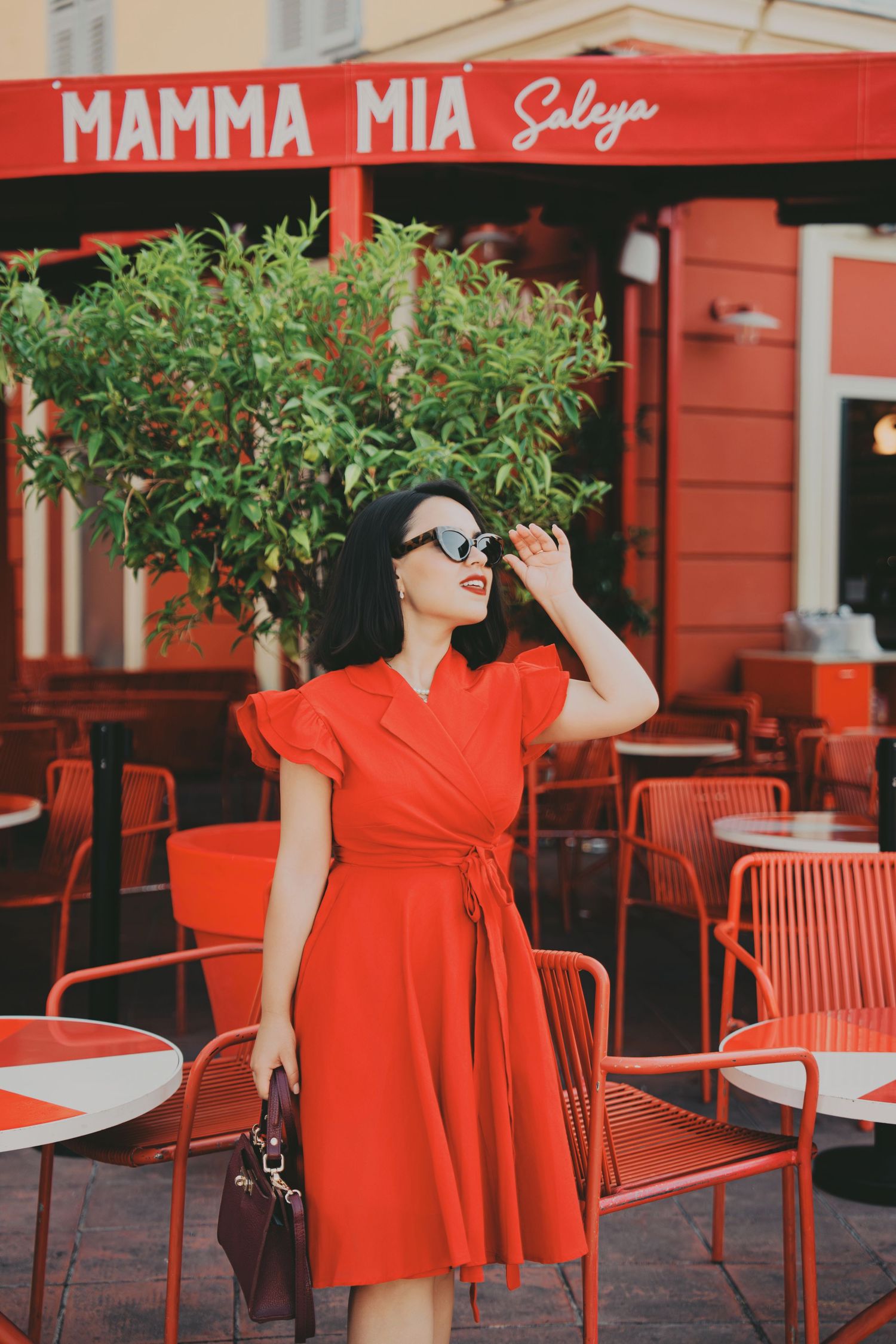Fashionable woman in red dress adjusting sunglasses outside Mamma Mia Saleya restaurant.