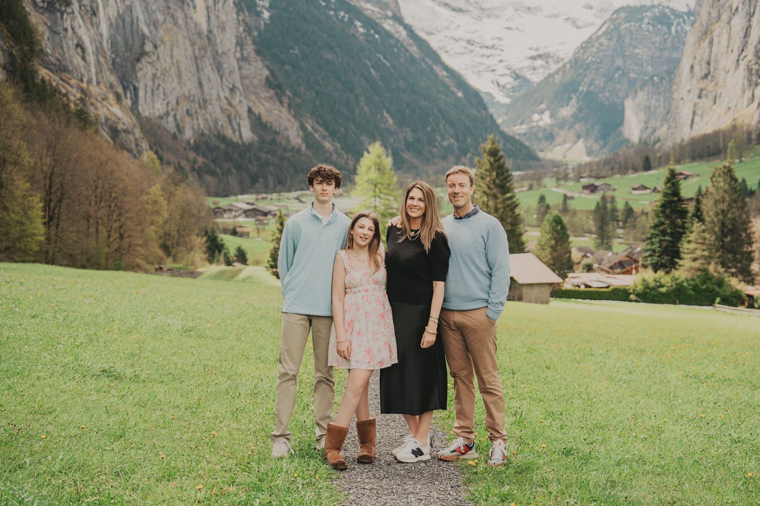Family of four posing together on a grassy hillside with the stunning Lauterbrunnen valley and Alps behind.