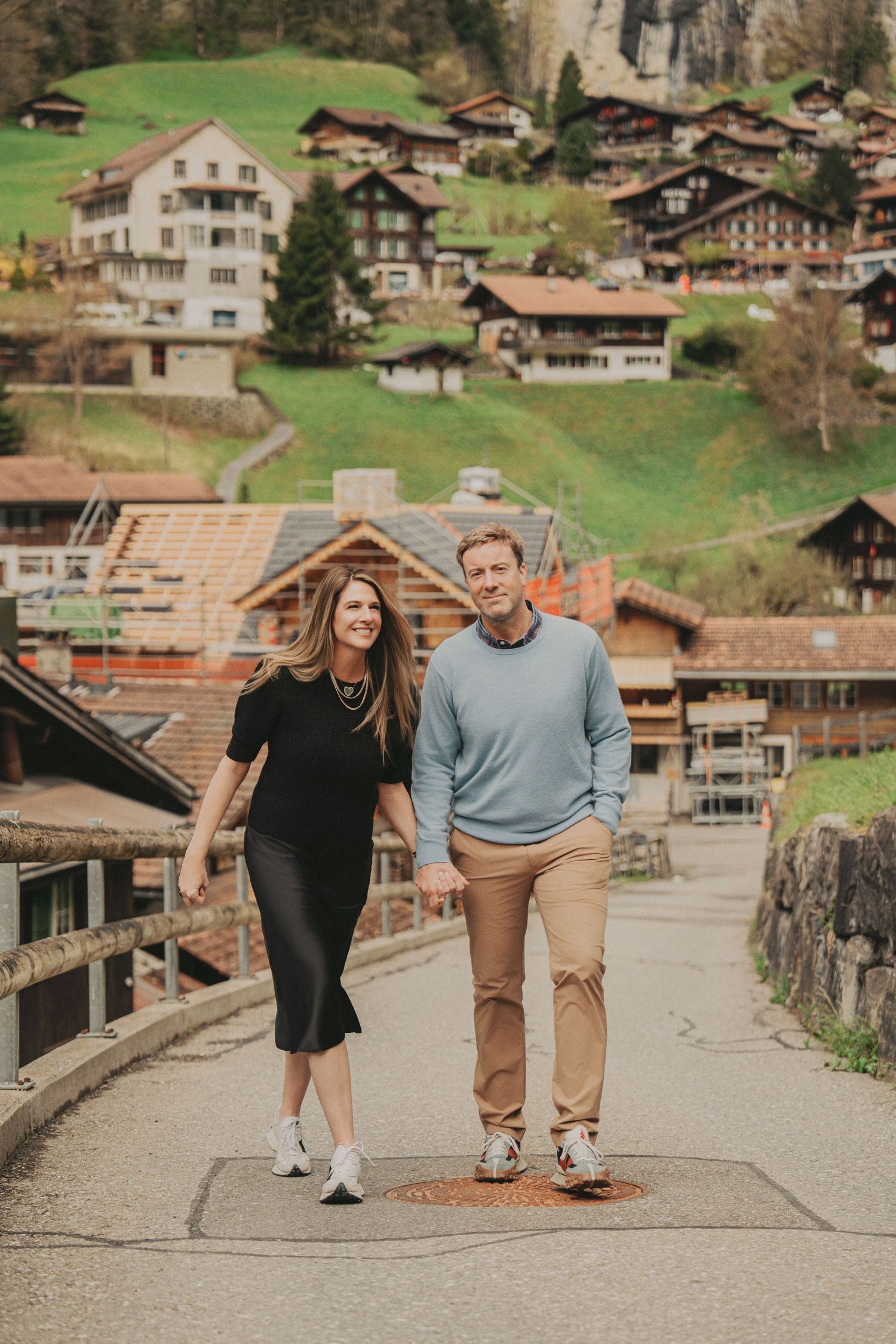 Couple holding hands walking down a road through a picturesque Swiss mountain village together.