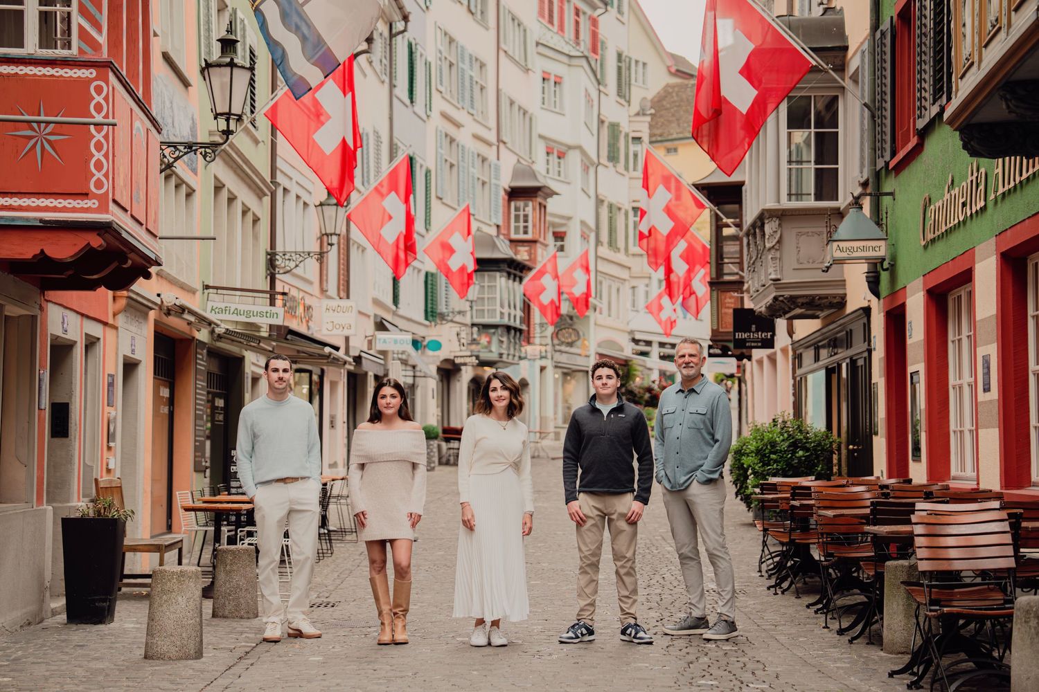 Group of five people posing in a cobblestone street decorated with Swiss flags in old town Zurich.