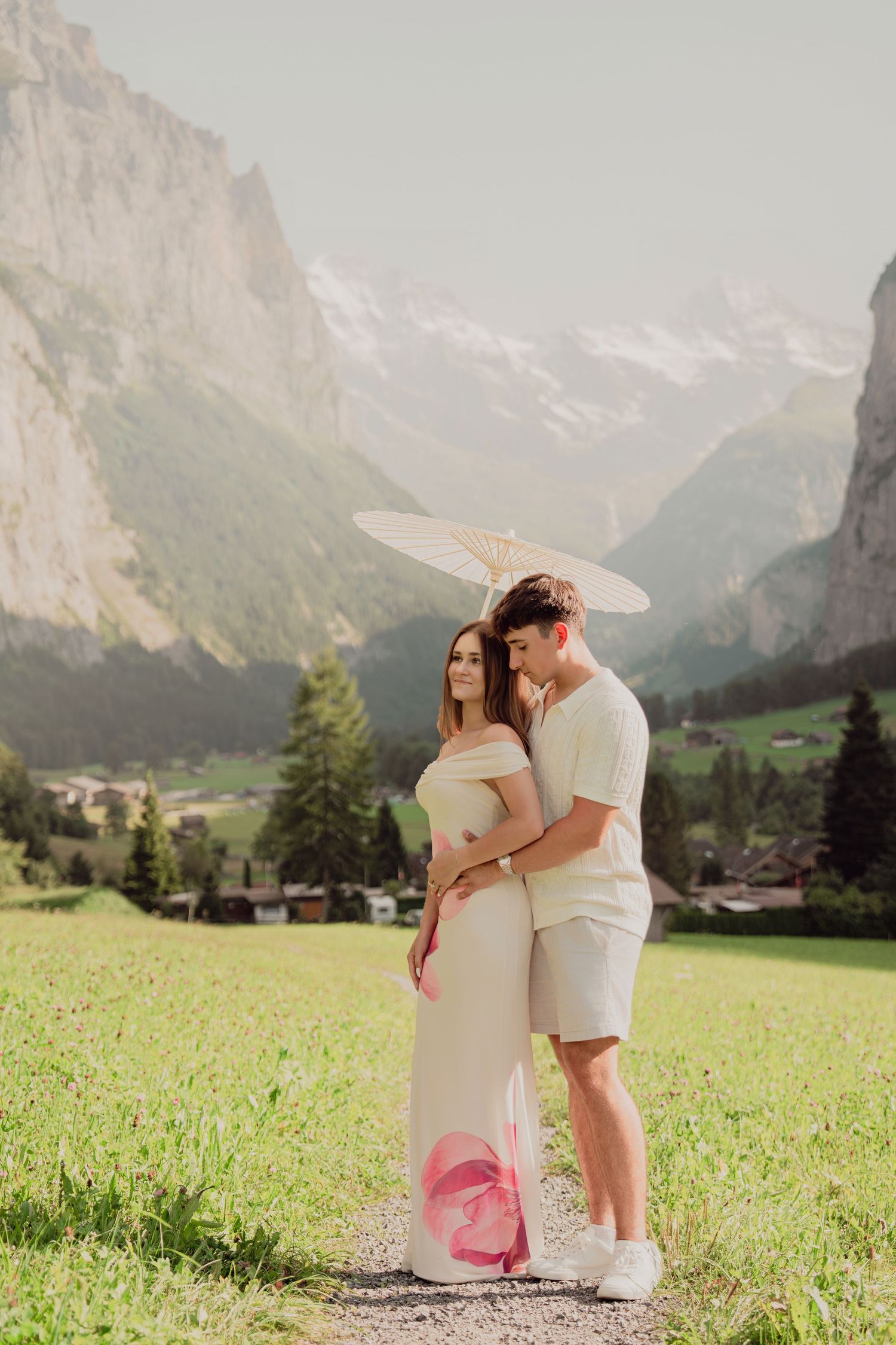 Romantic couple embracing on a path in Lauterbrunnen, Switzerland, woman holding a parasol umbrella.