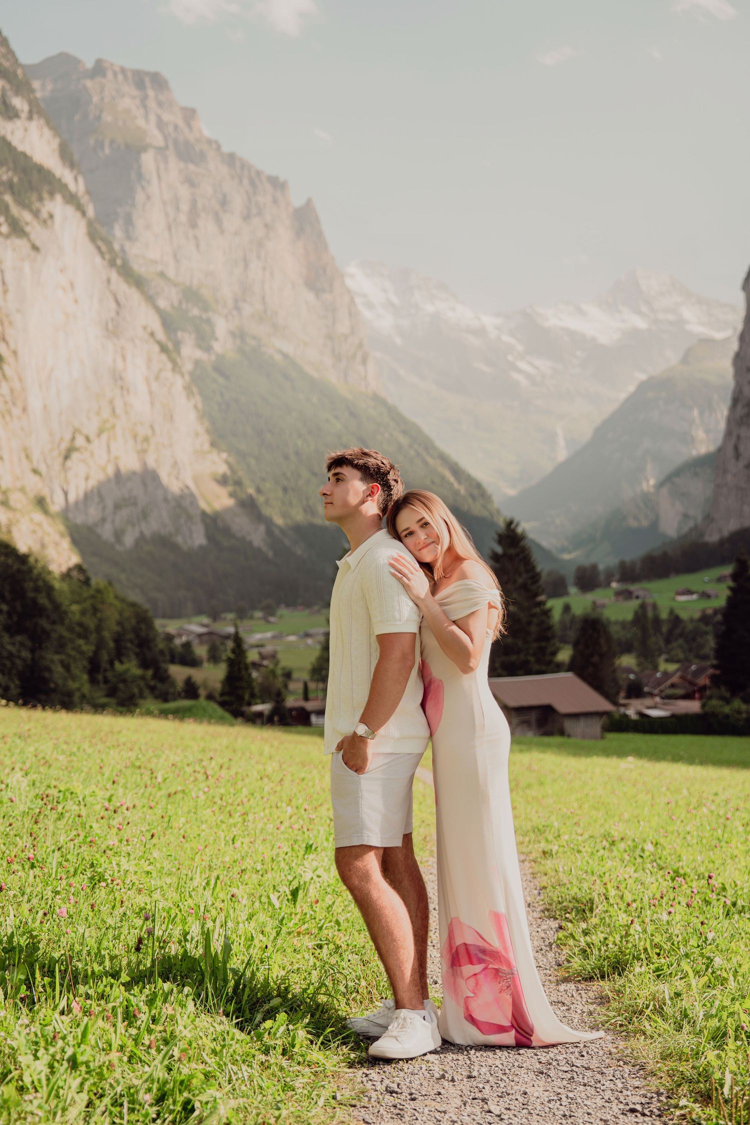Couple standing close together on a gravel path in a scenic Swiss alpine valley landscape.