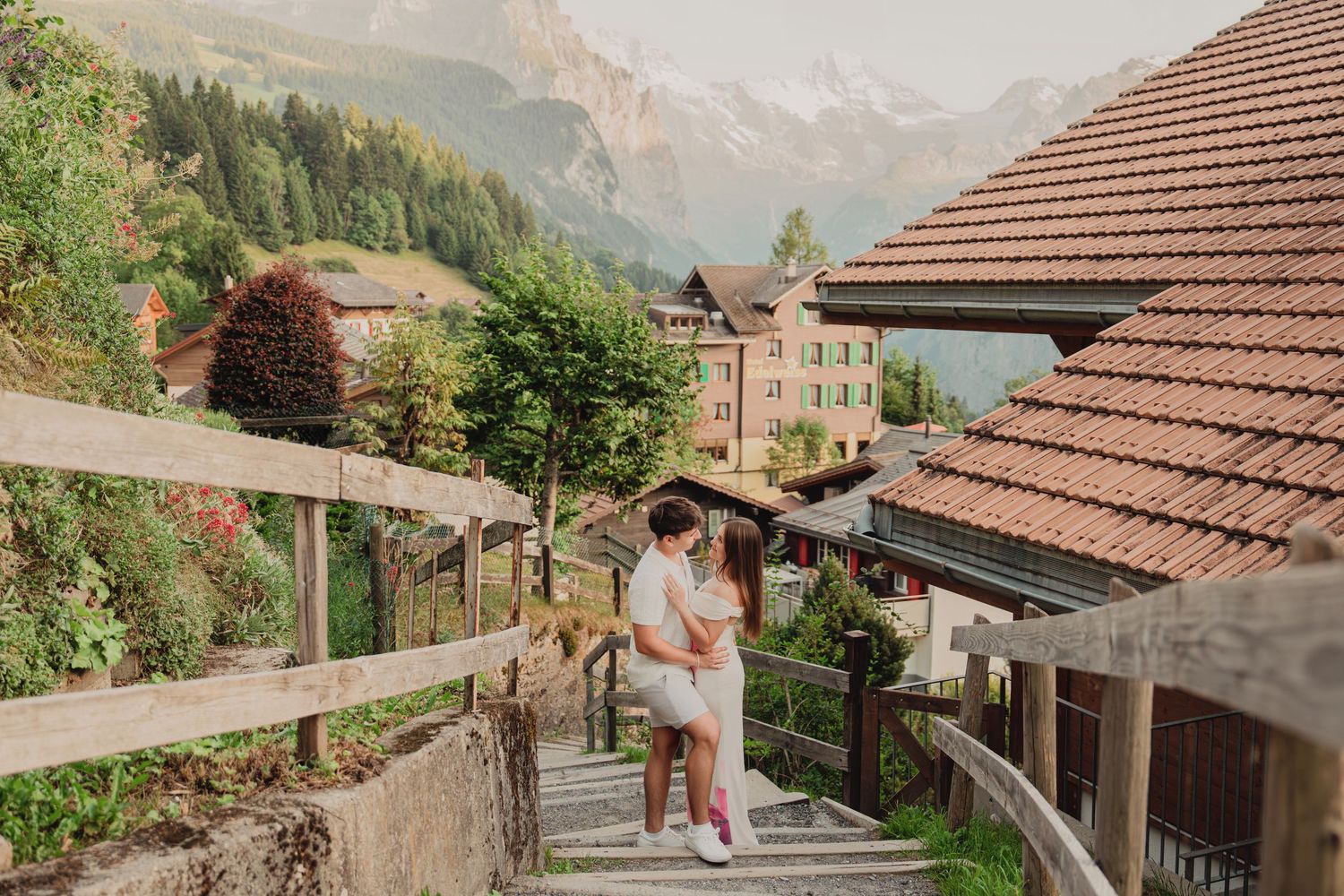 Romantic couple sitting together on rustic wooden stairs in a scenic Swiss Alpine village with mountain views.