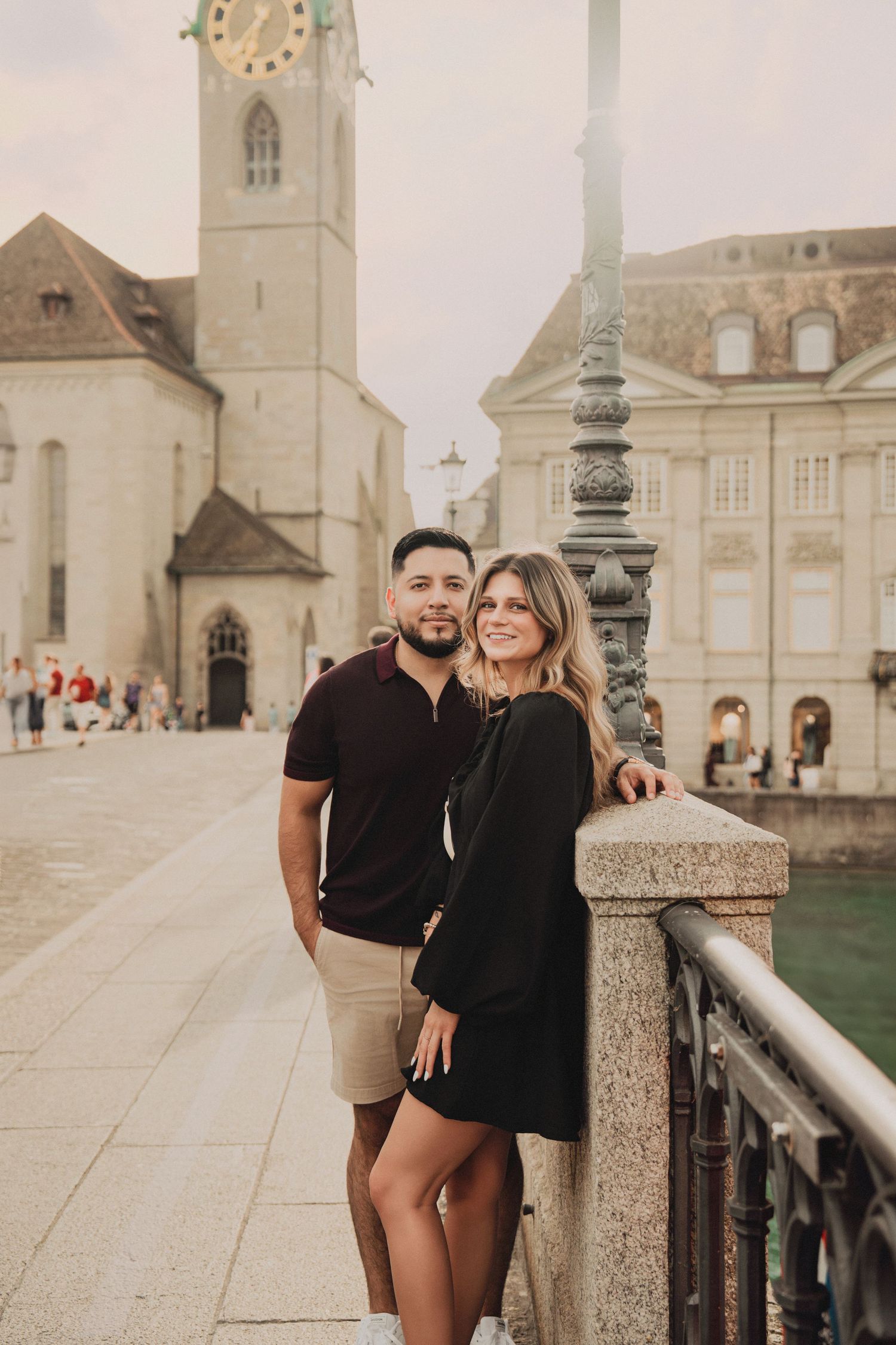 Couple posing on a bridge in Zurich old town with historic church tower backdrop.