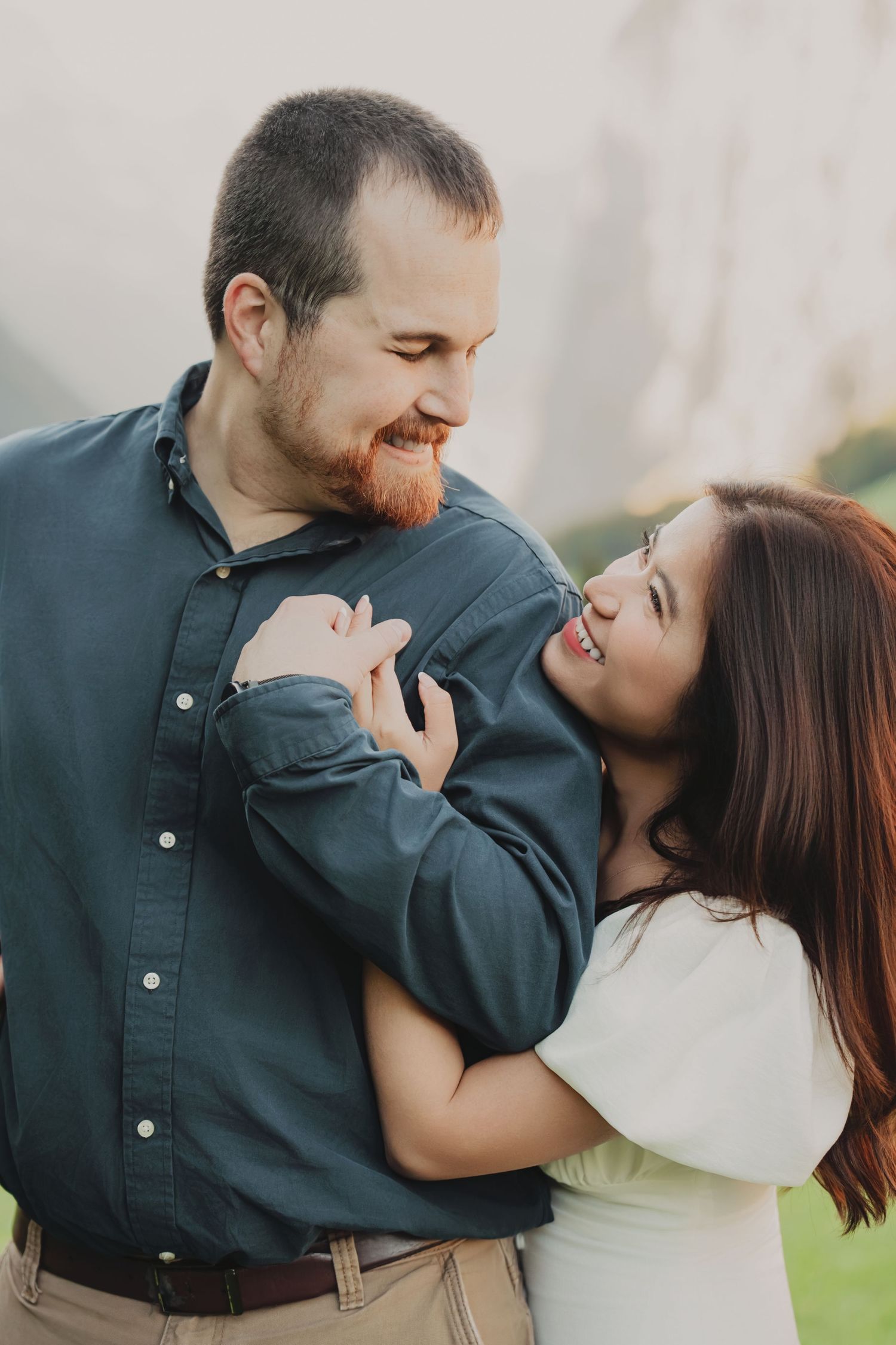 Couple sharing a warm smile while embracing in a scenic outdoor location.