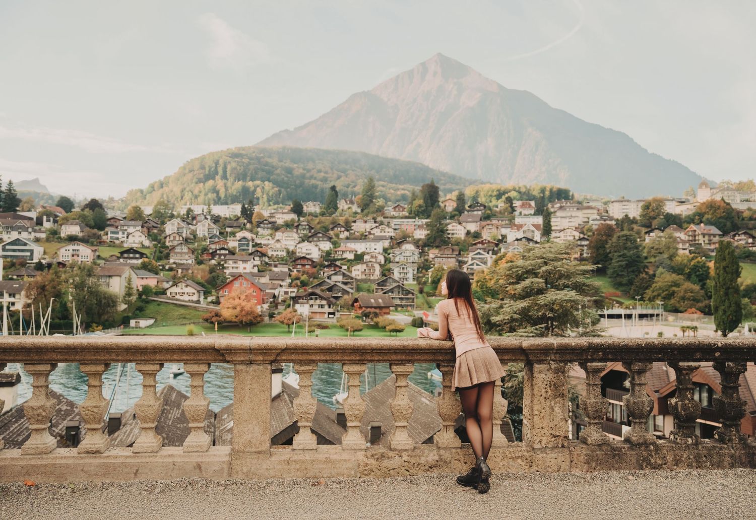 Woman posing by stone balustrade with stunning Swiss village and dramatic mountain in background.
