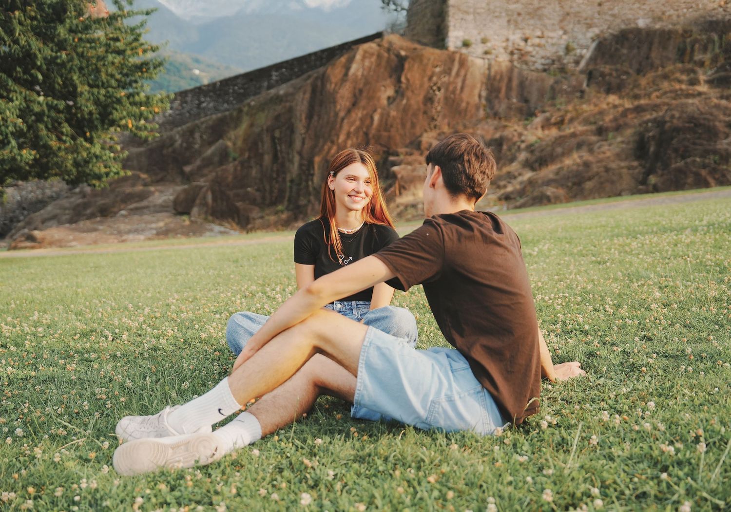 Young couple sitting together on grass smiling with rocky mountain scenery behind.