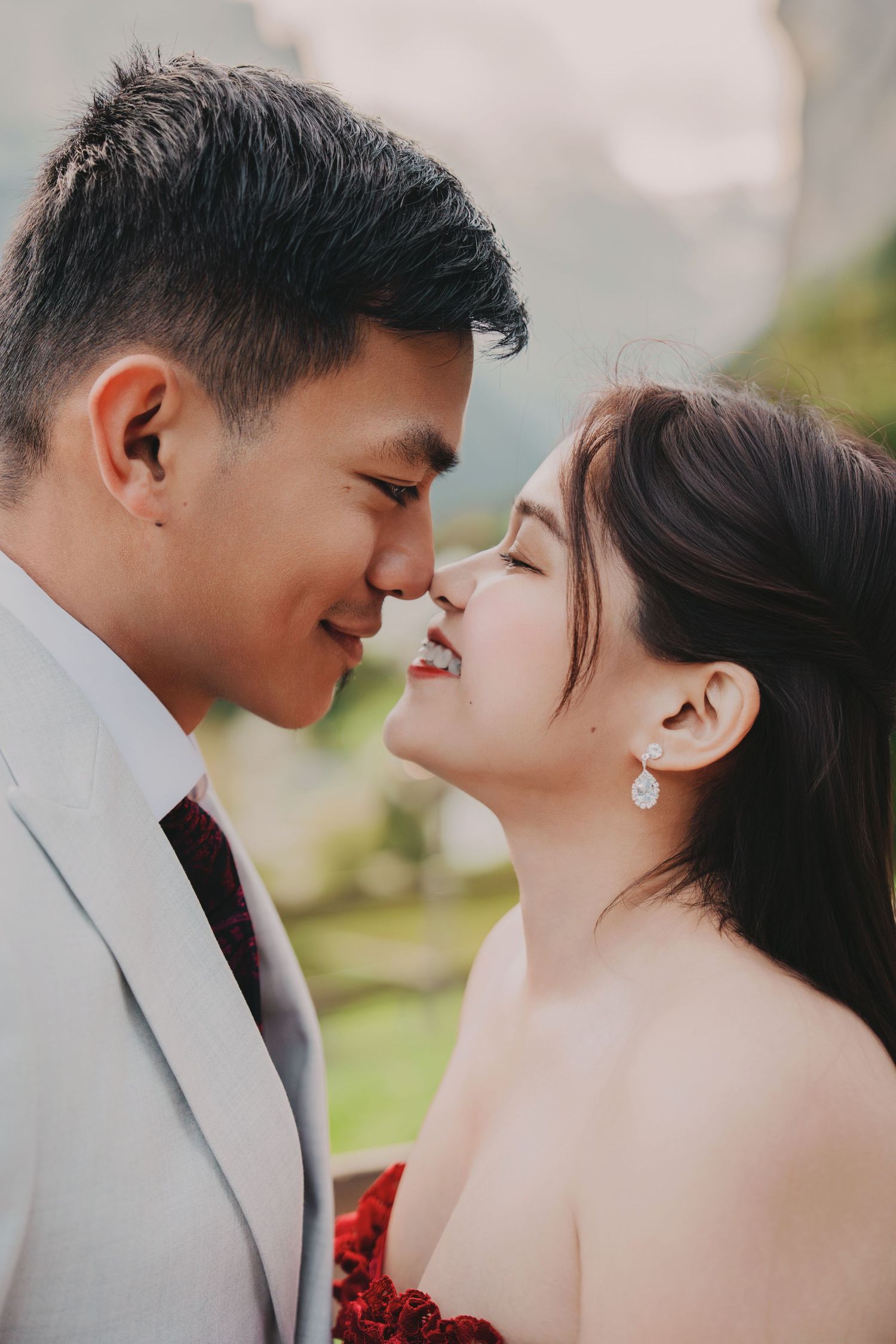 Close romantic moment of a smiling couple nearly kissing outdoors with a soft bokeh alpine background.