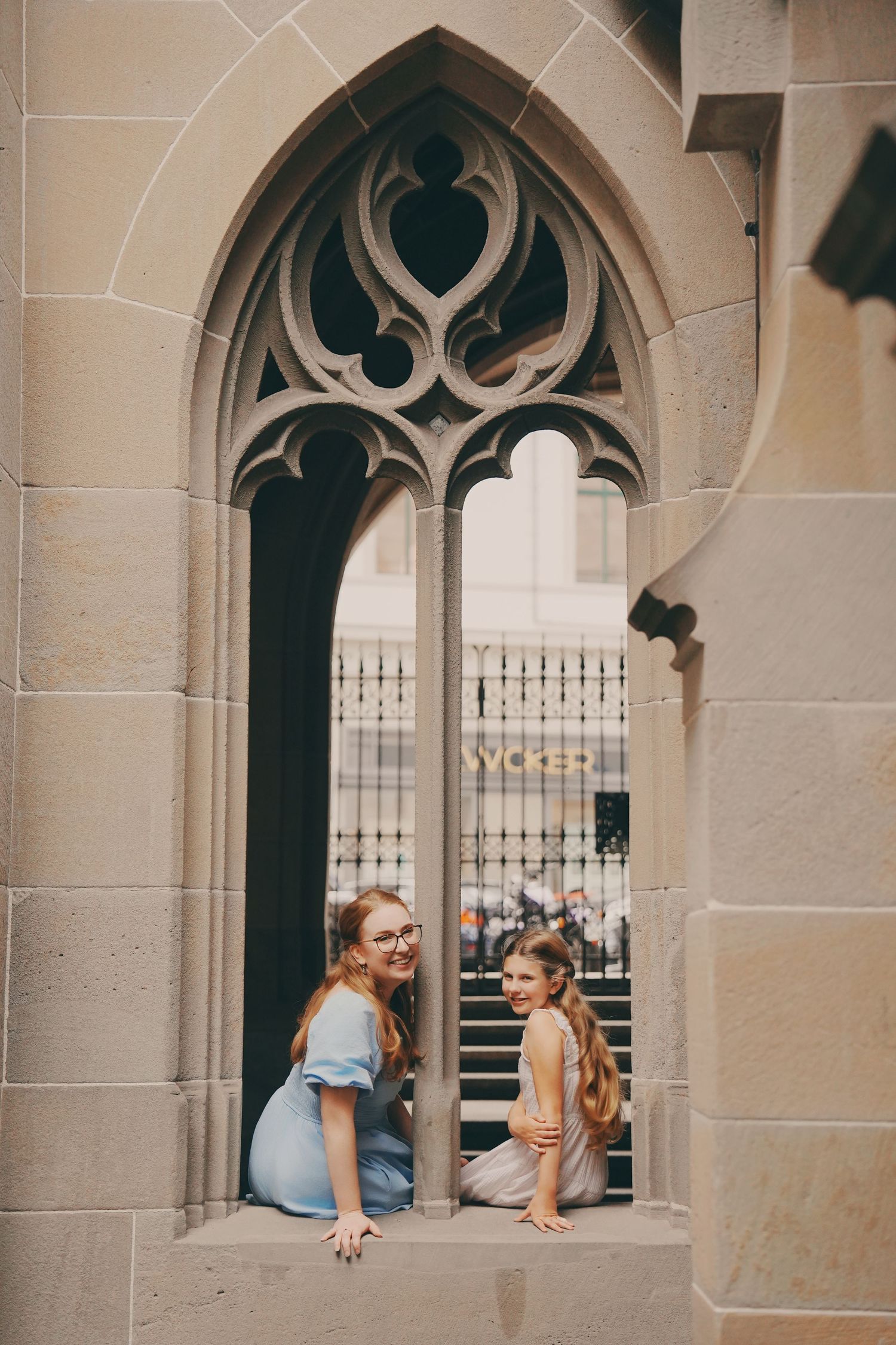 Mother and daughter posing in decorative Gothic stone arch window of historic cathedral.