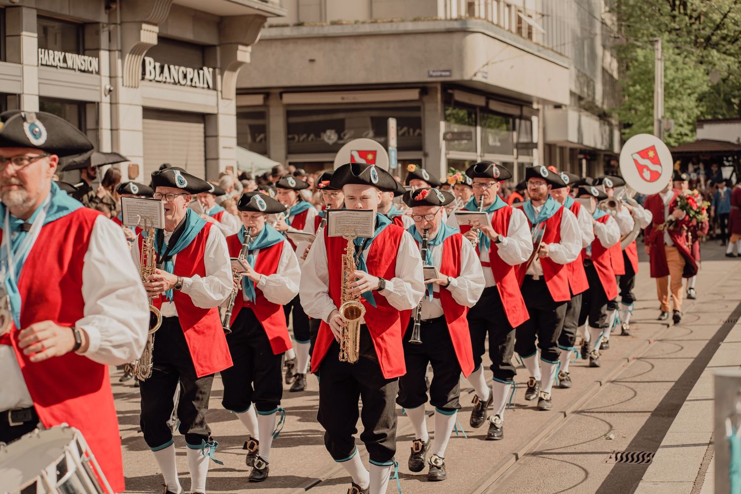 Marching band in red and white traditional costumes playing saxophones during an outdoor city street parade.