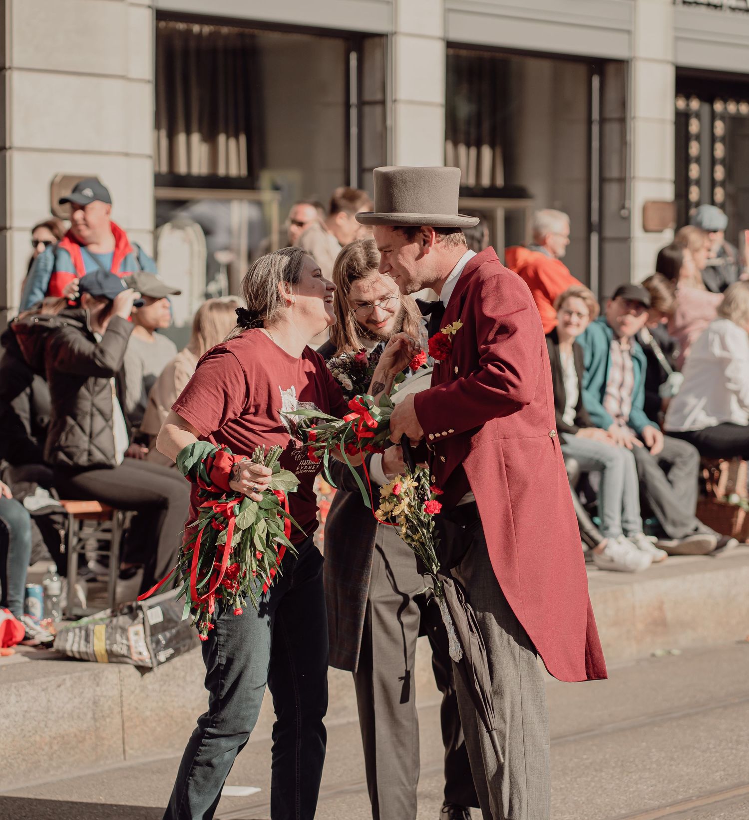 People in vintage red costumes exchange roses at an outdoor festival event on a sunny day.