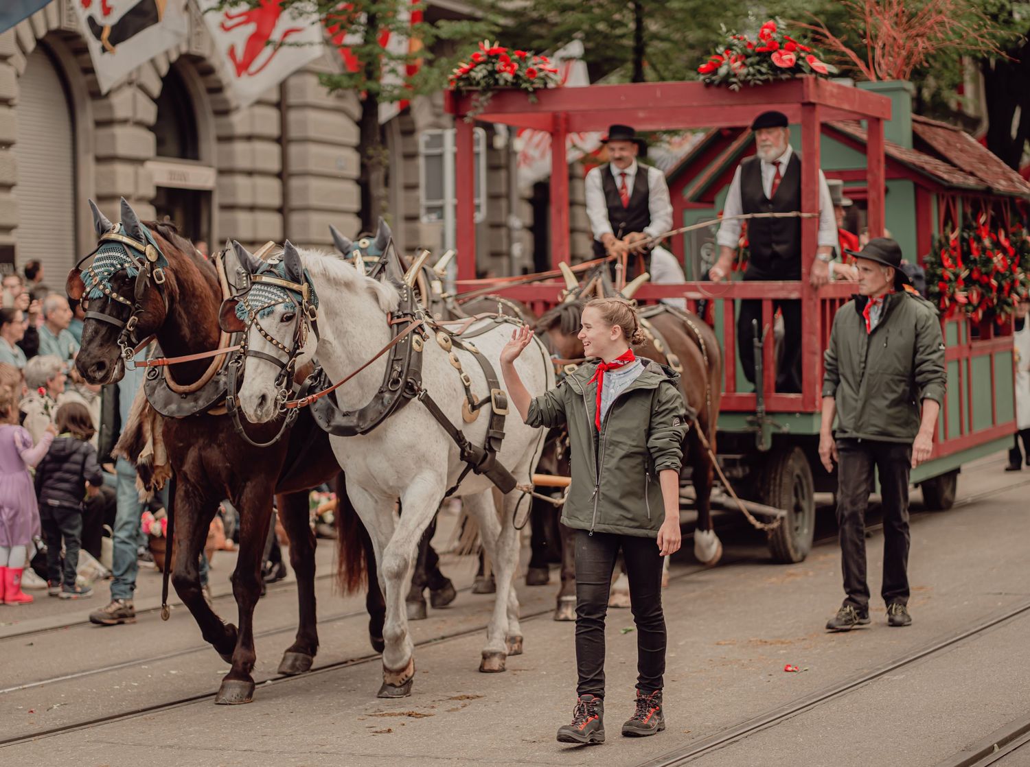 Horse-drawn red carriage with handlers guides through a festive Swiss cultural street parade.