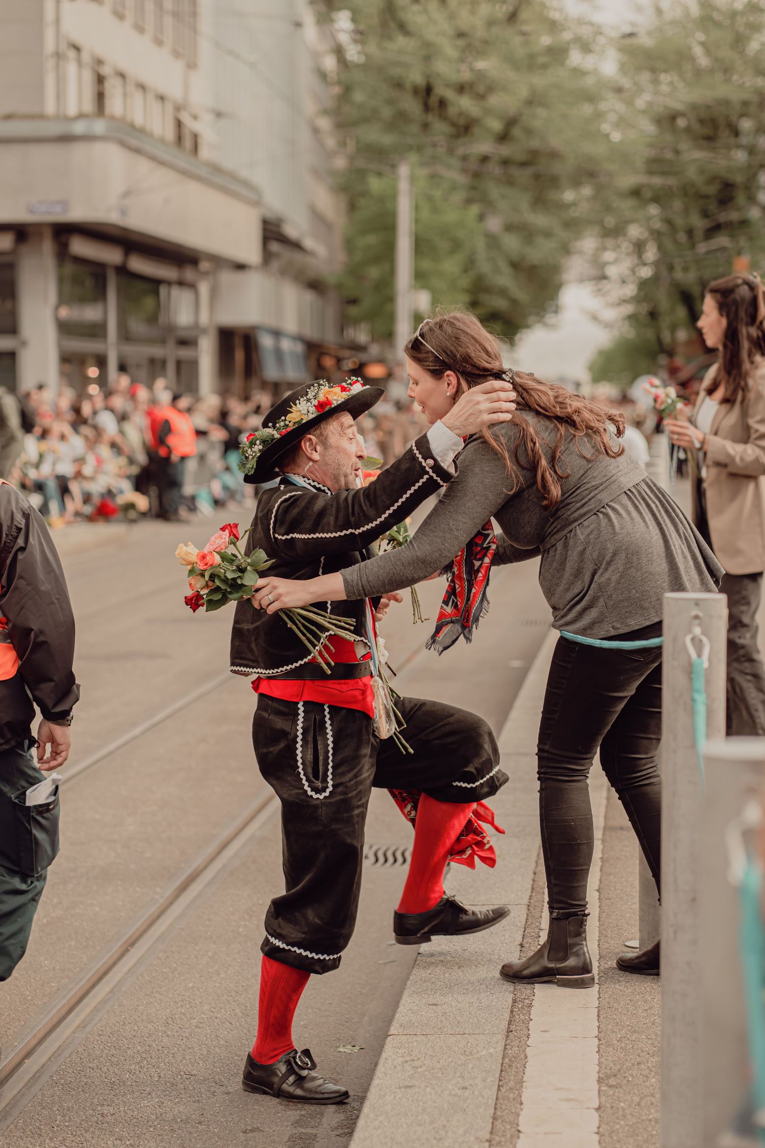 Man in traditional black and red Swiss costume playfully interacts with a woman at a street parade.