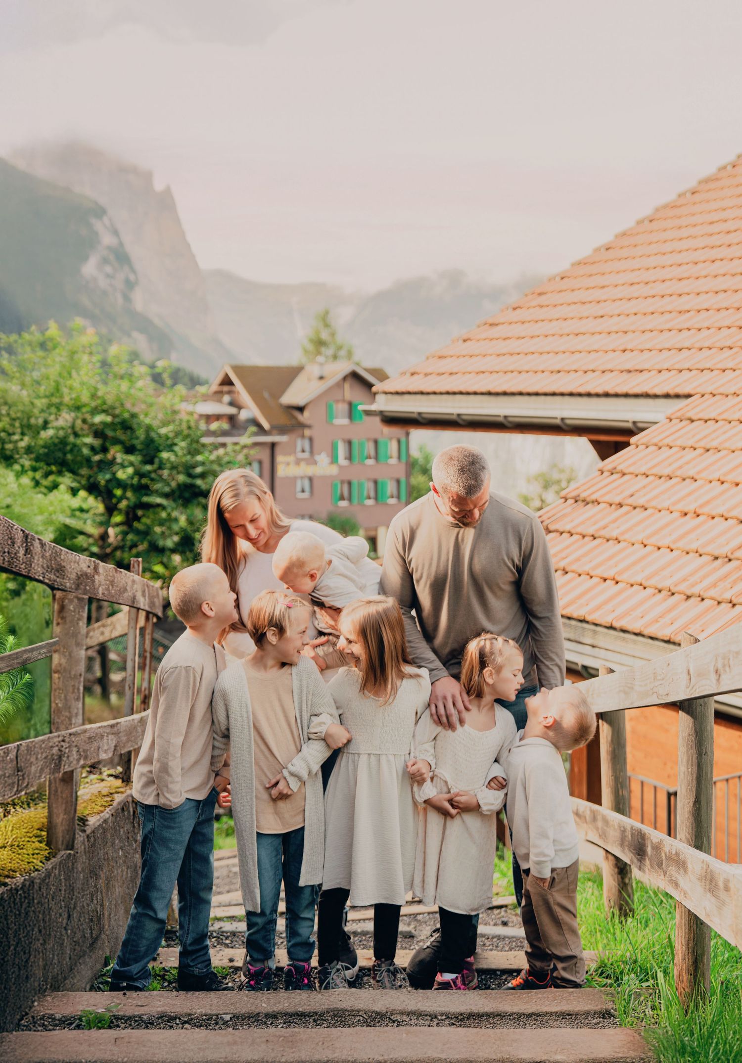 Large family with parents and eight children gathered on wooden steps in a Swiss mountain village.