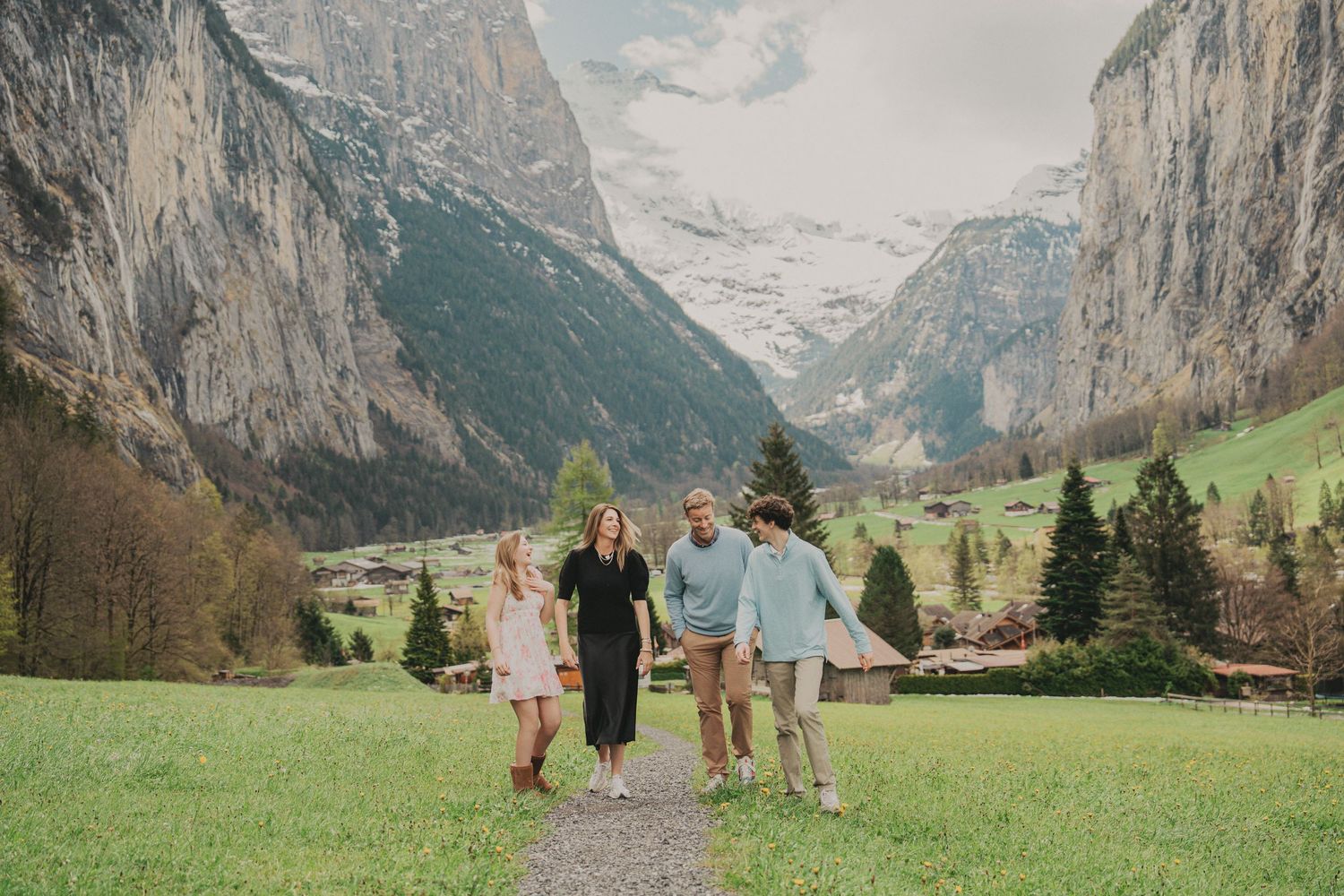 Family of four walking along a path in Lauterbrunnen with snow-capped Swiss Alps and green valley views.