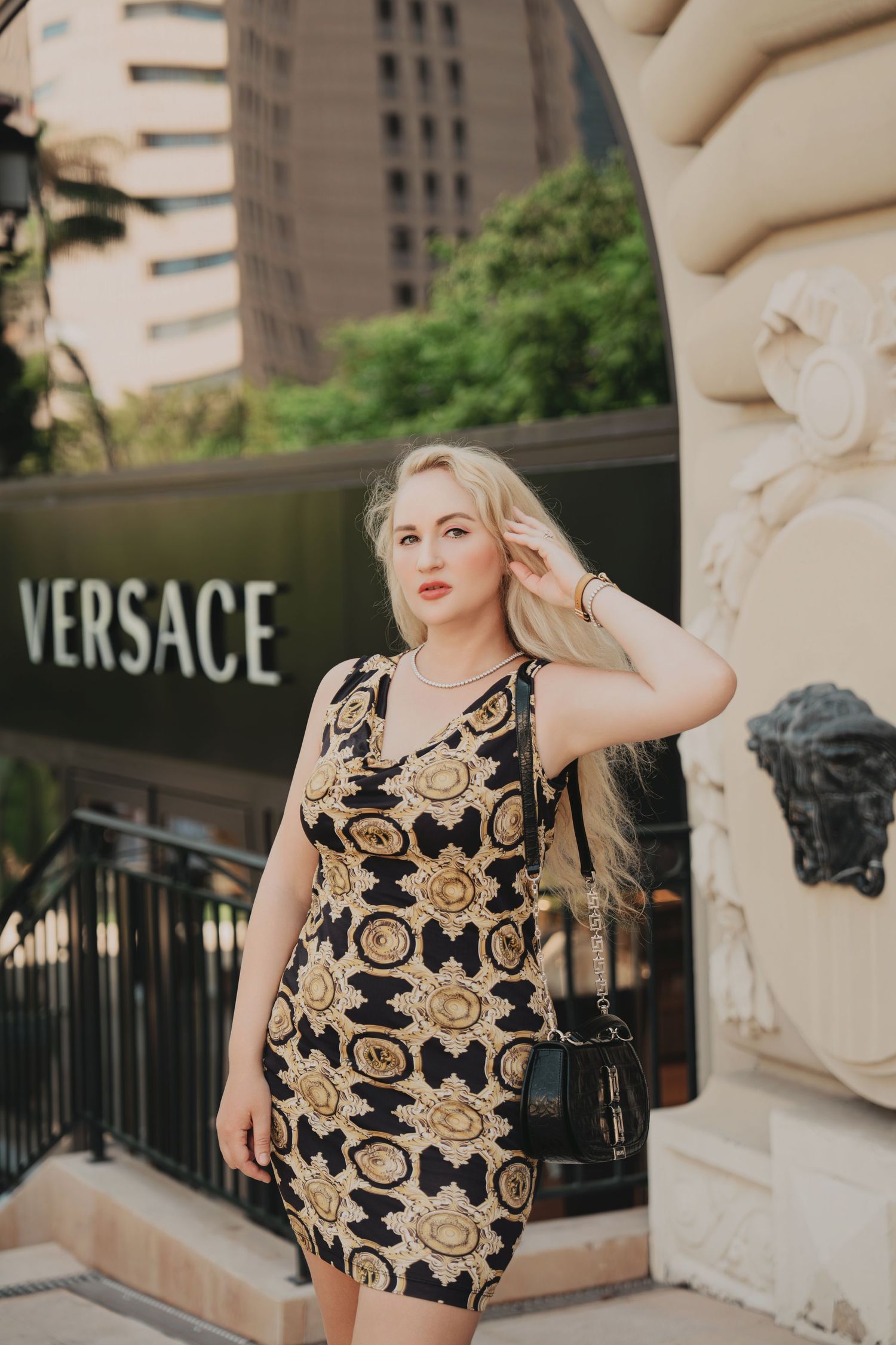 Blonde woman in black and gold Versace mini dress posing outside Versace store Monaco.