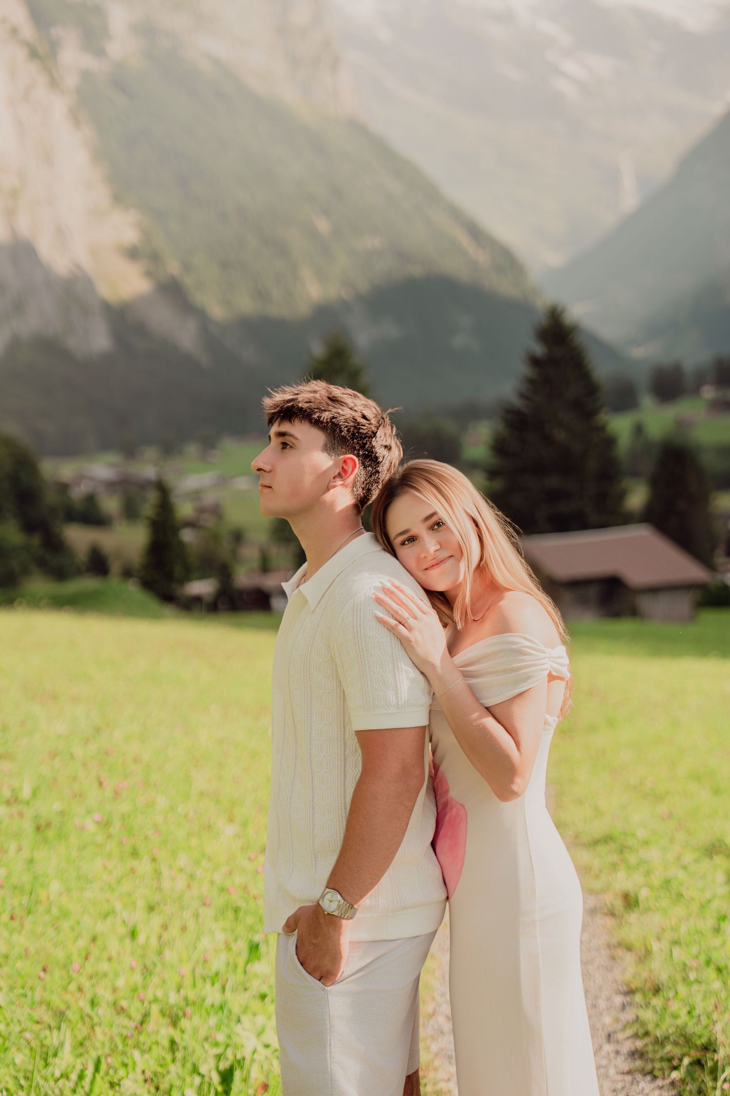Young couple embracing in a sunny alpine meadow with majestic mountain peaks in Switzerland.