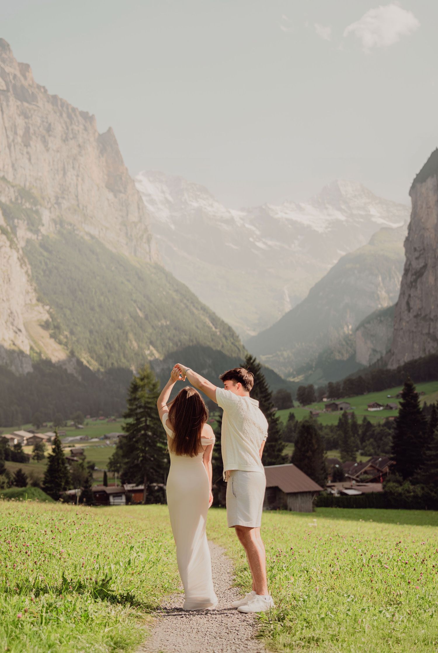 Couple dancing with raised arms on a meadow path with panoramic view of the stunning Lauterbrunnen valley.