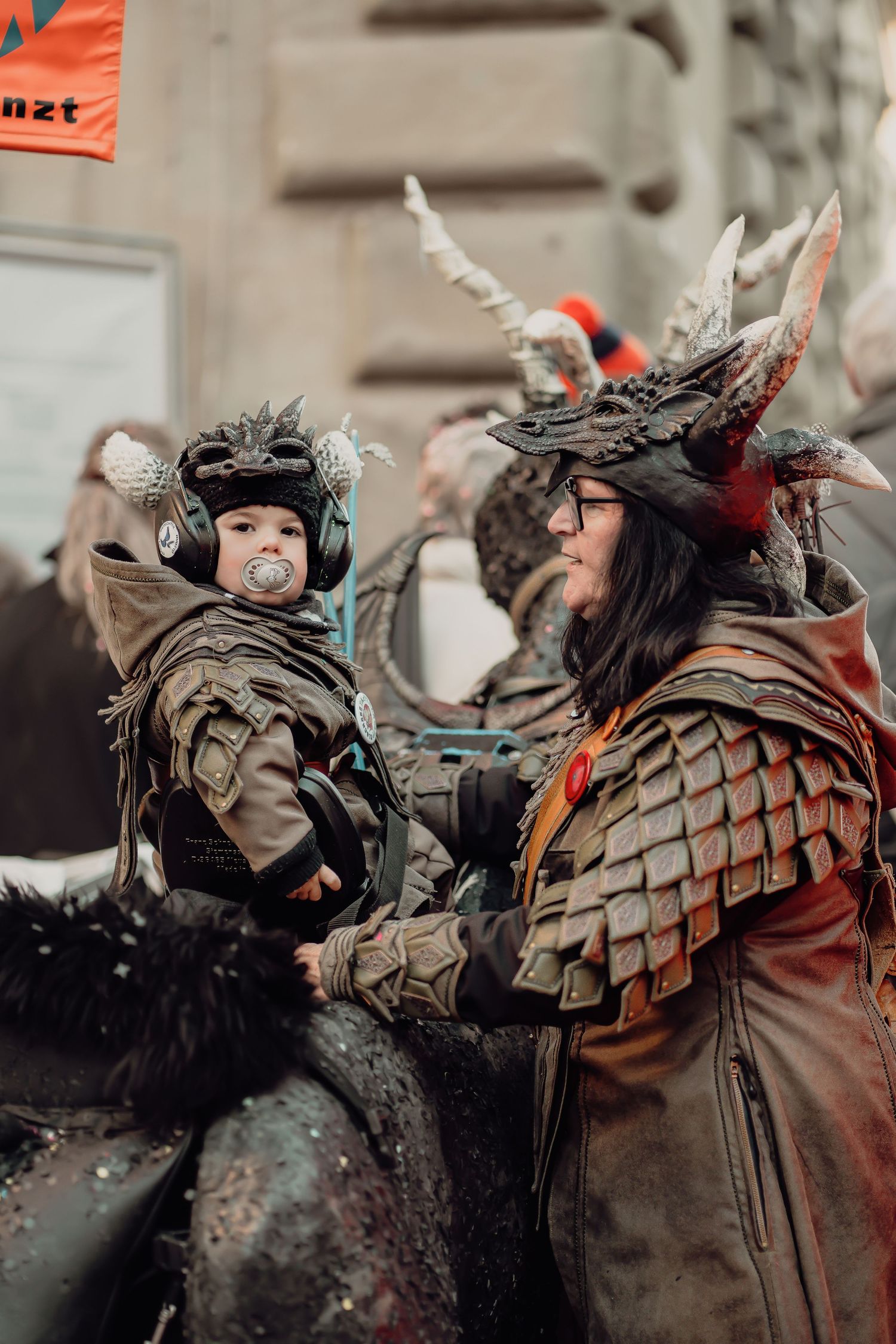 Adult and baby both dressed in dragon armor costumes at a carnival street parade.