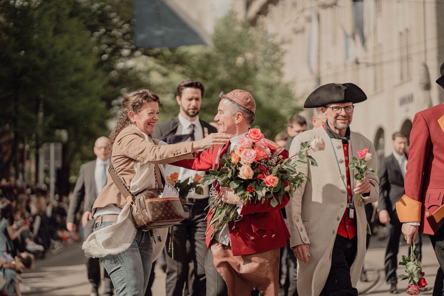 Man in historical costume shares flowers with a woman spectator during a festive street parade.