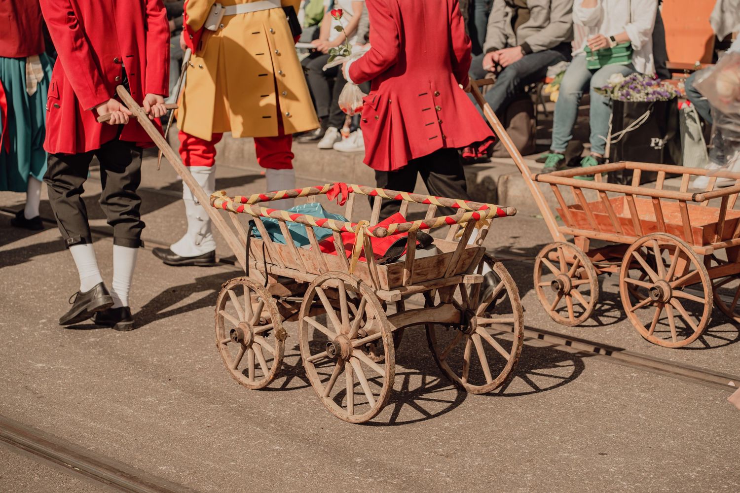 Colorful wooden cart decorated with flowers pulled by performers in historical red costumes during a street parade.