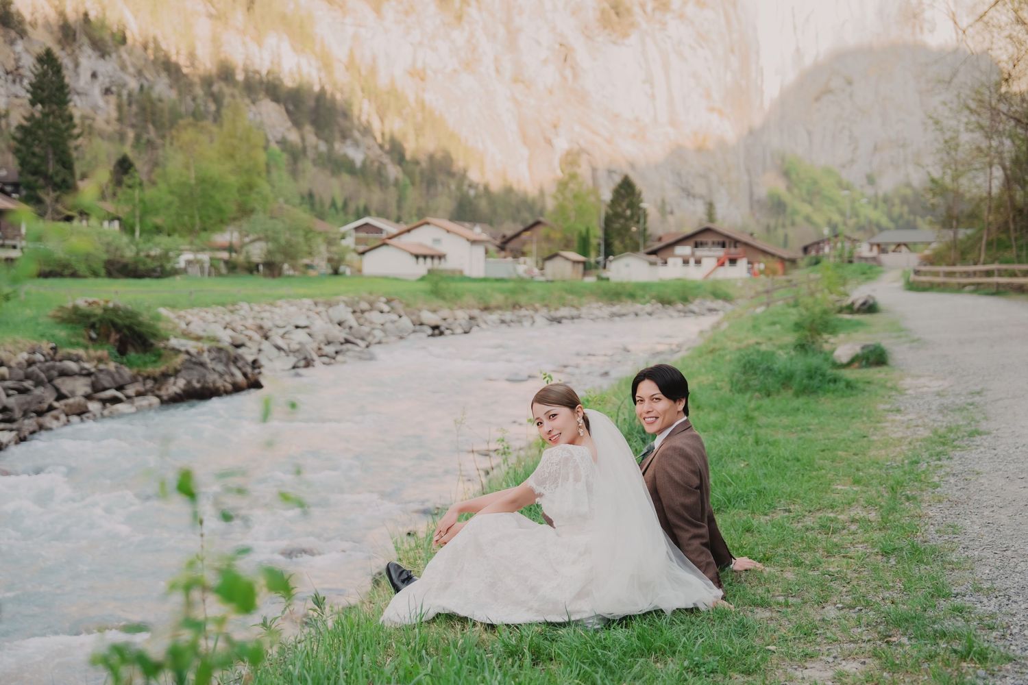Couple in wedding attire sitting by a mountain river in Lauterbrunnen, Switzerland.